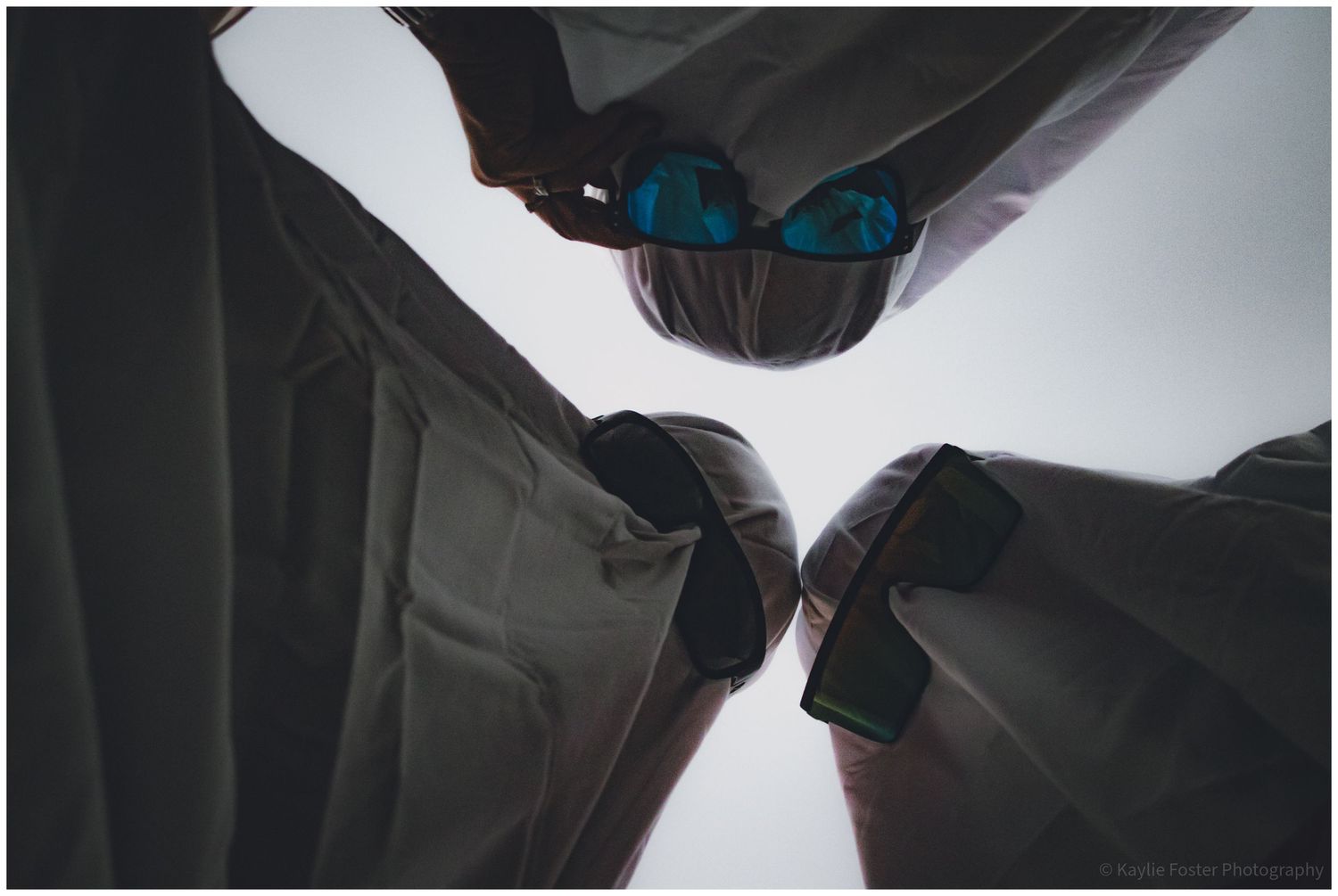 Low-angle view of three people in dress shirts huddle together, one wearing blue mirrored sunglasses.
