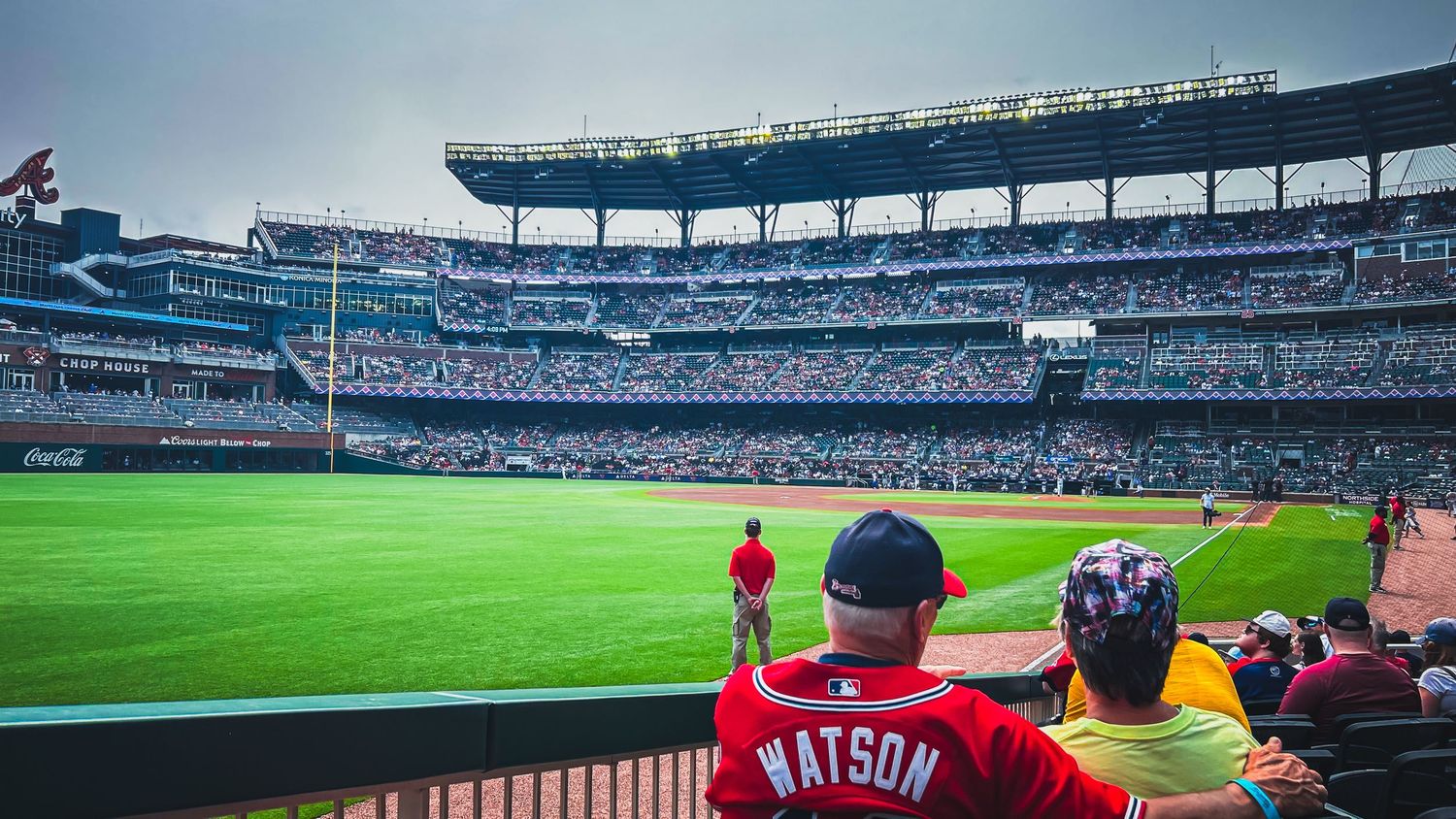 Fans watch a baseball game from the stands at a packed MLB stadium, with a player named Watson visible in the crowd.