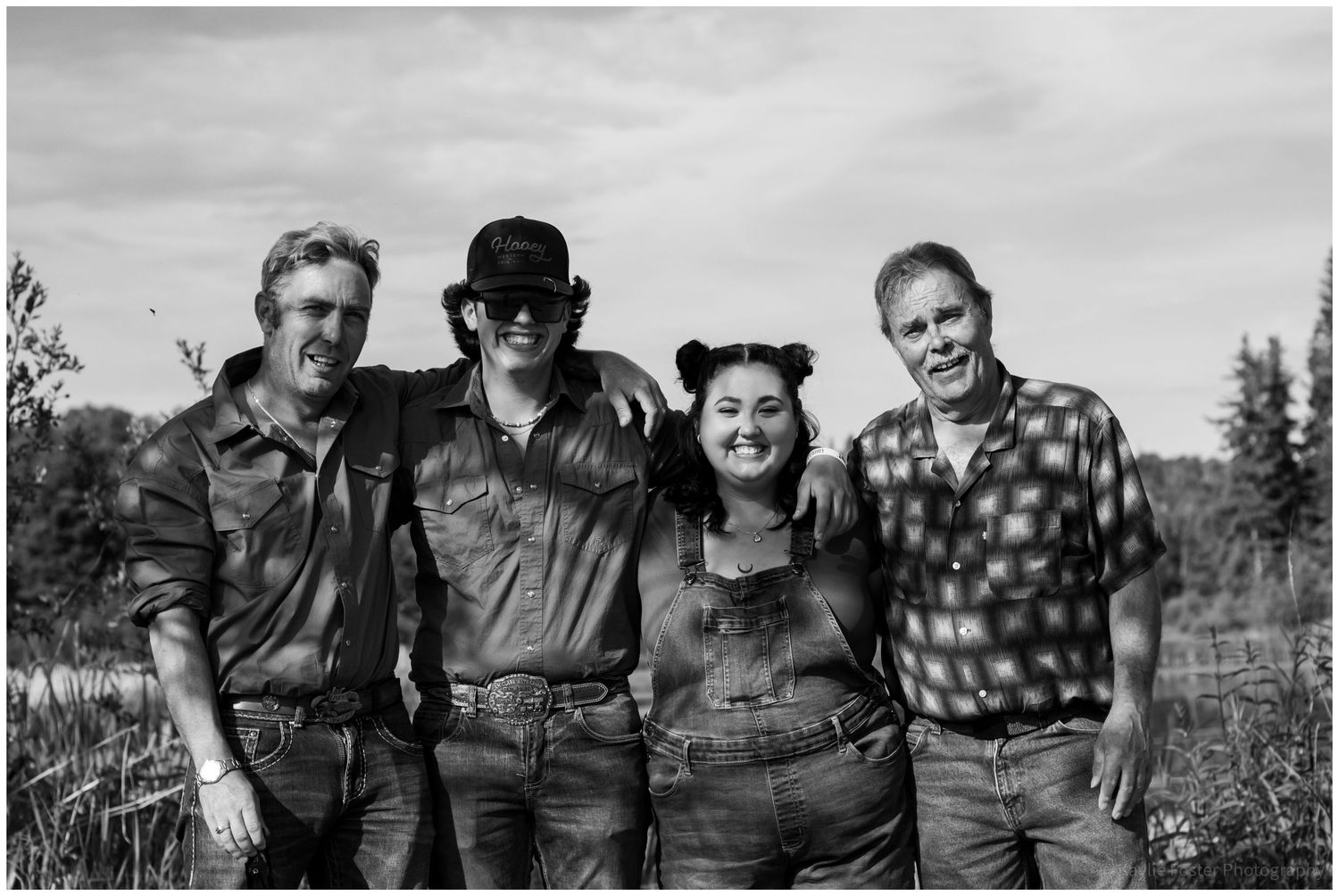 Four friends smile together outdoors in a rural setting, posing for a black and white group photo.