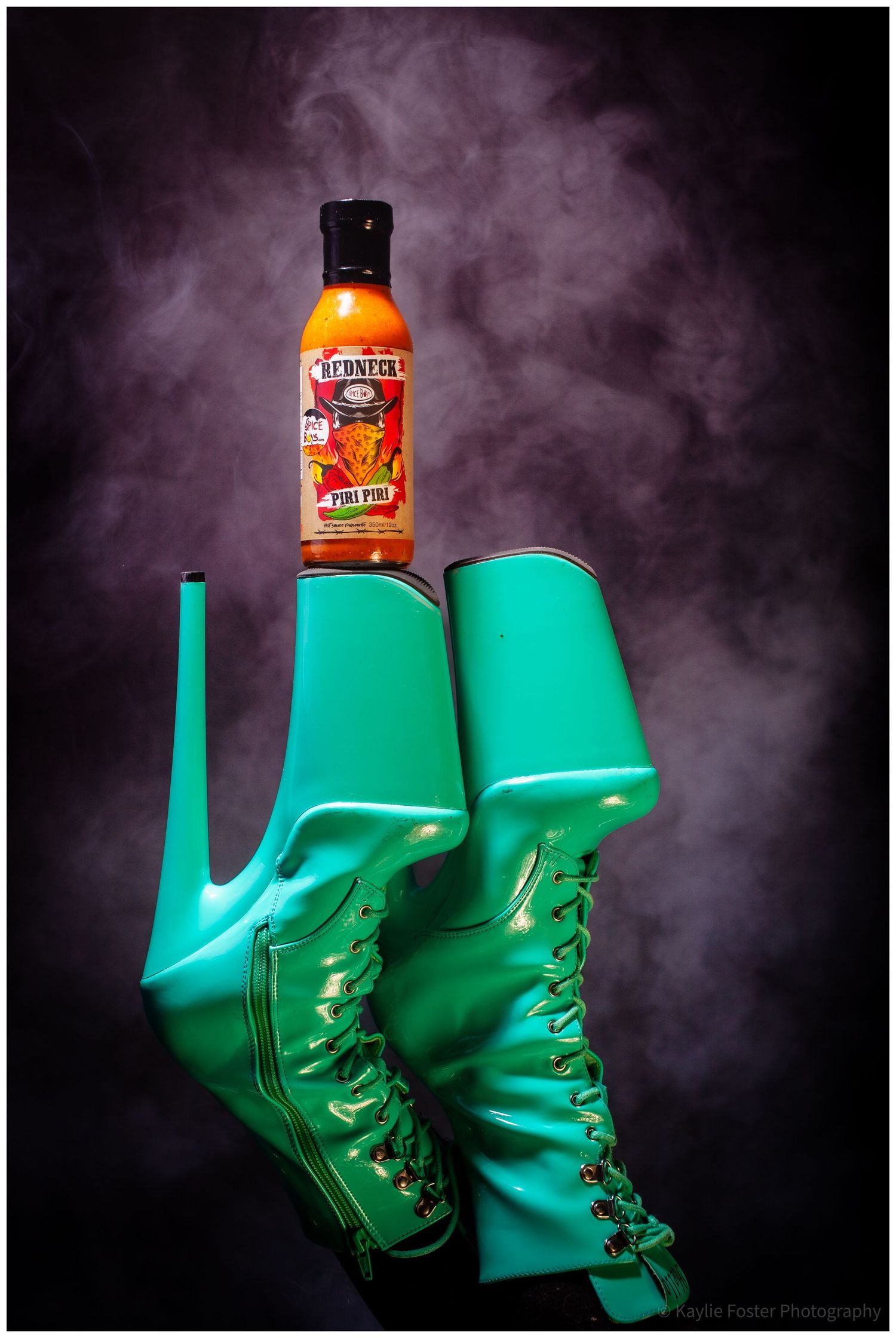 Teal lace-up platform boots displaying a Redneck Piri Piri hot sauce bottle on smoky background.