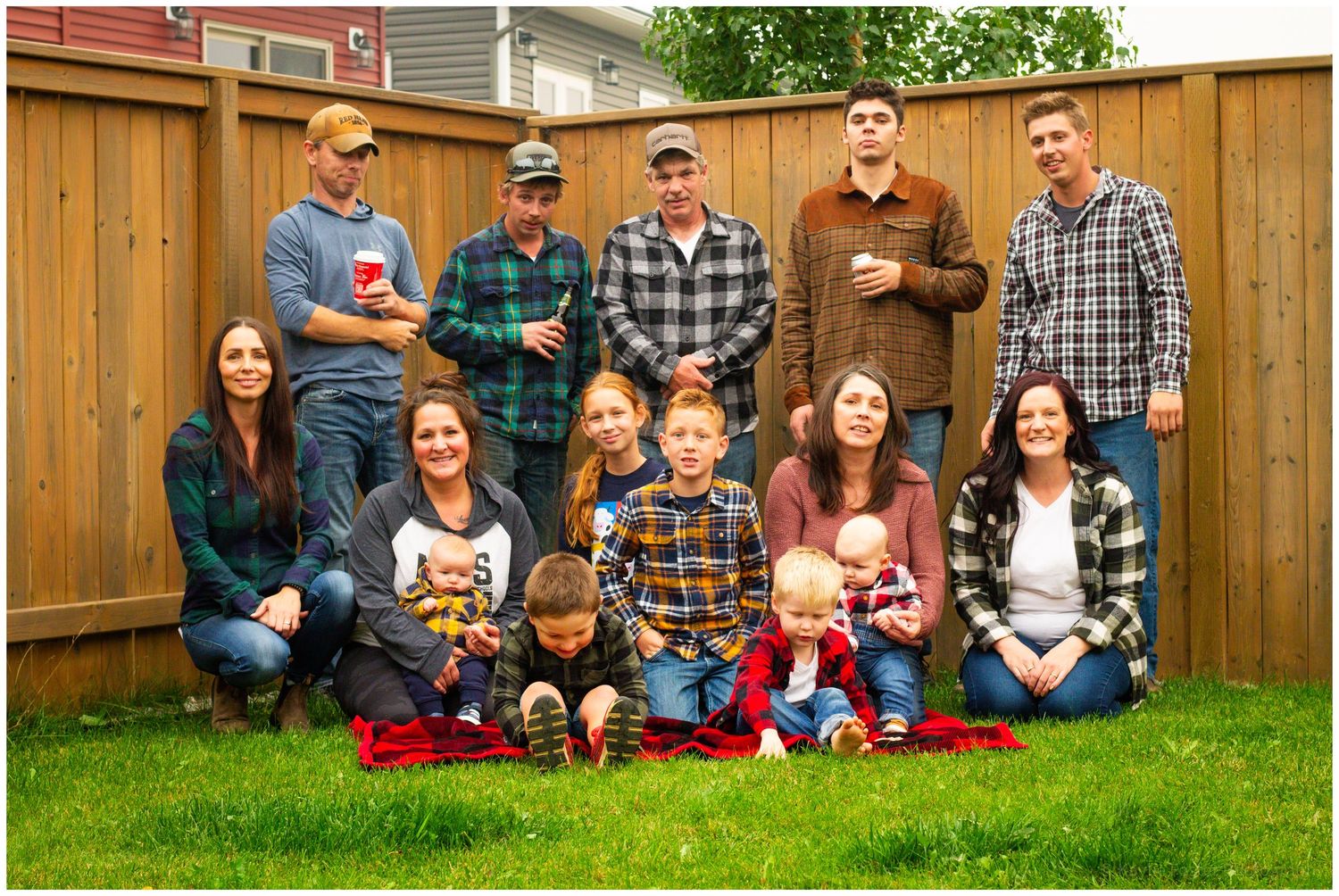 Large extended family group photo with adults and children posing in a backyard by a fence.