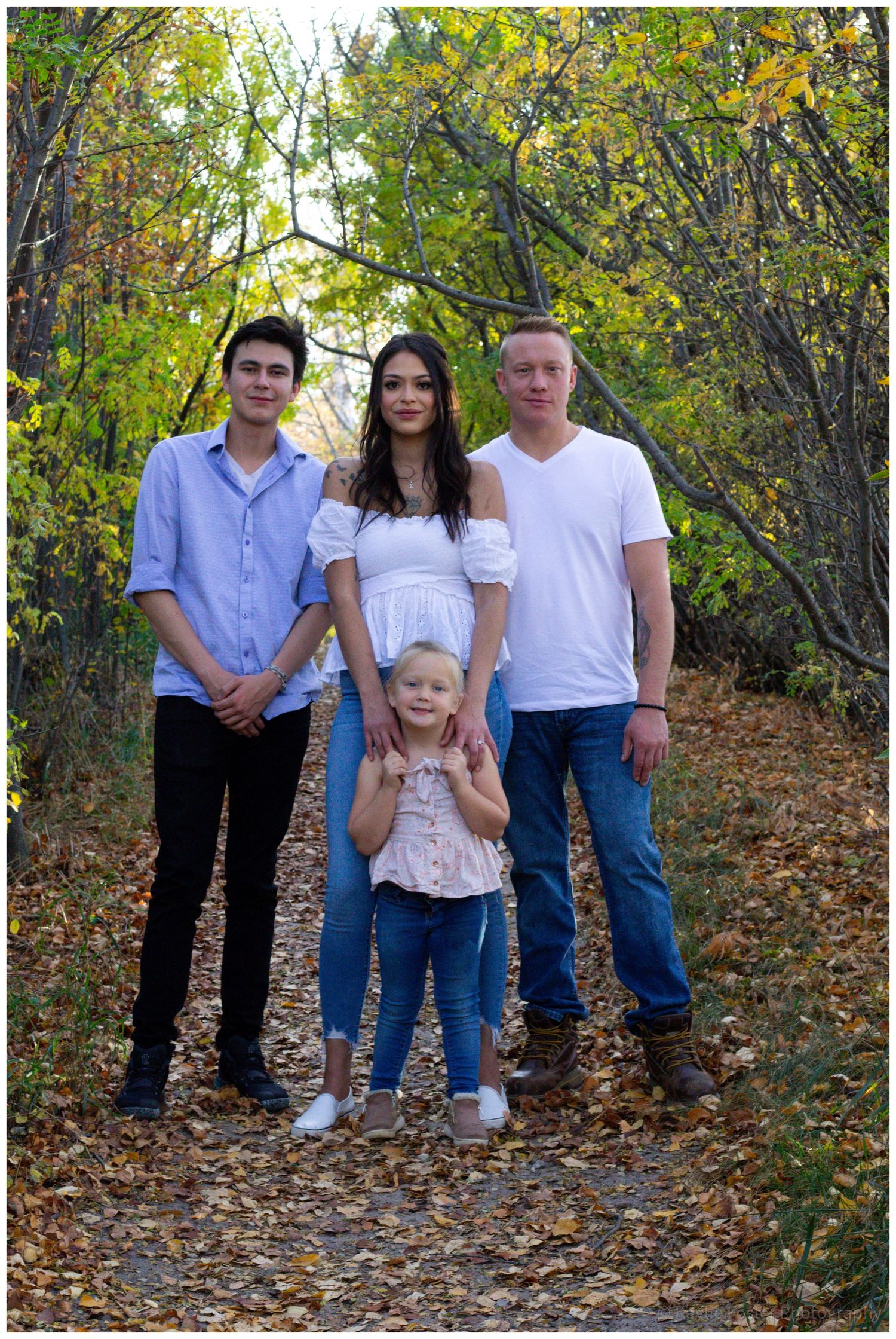 A family of four poses on a leaf-covered path surrounded by colorful autumn foliage.
