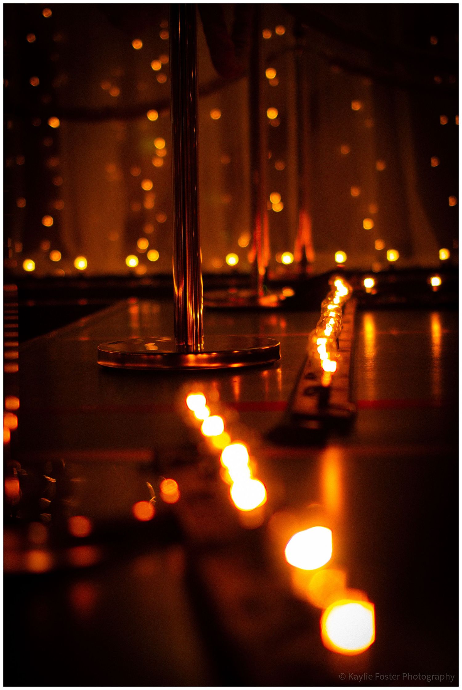 Elegant event venue with candles reflecting on a dark surface and warm bokeh fairy lights in background.