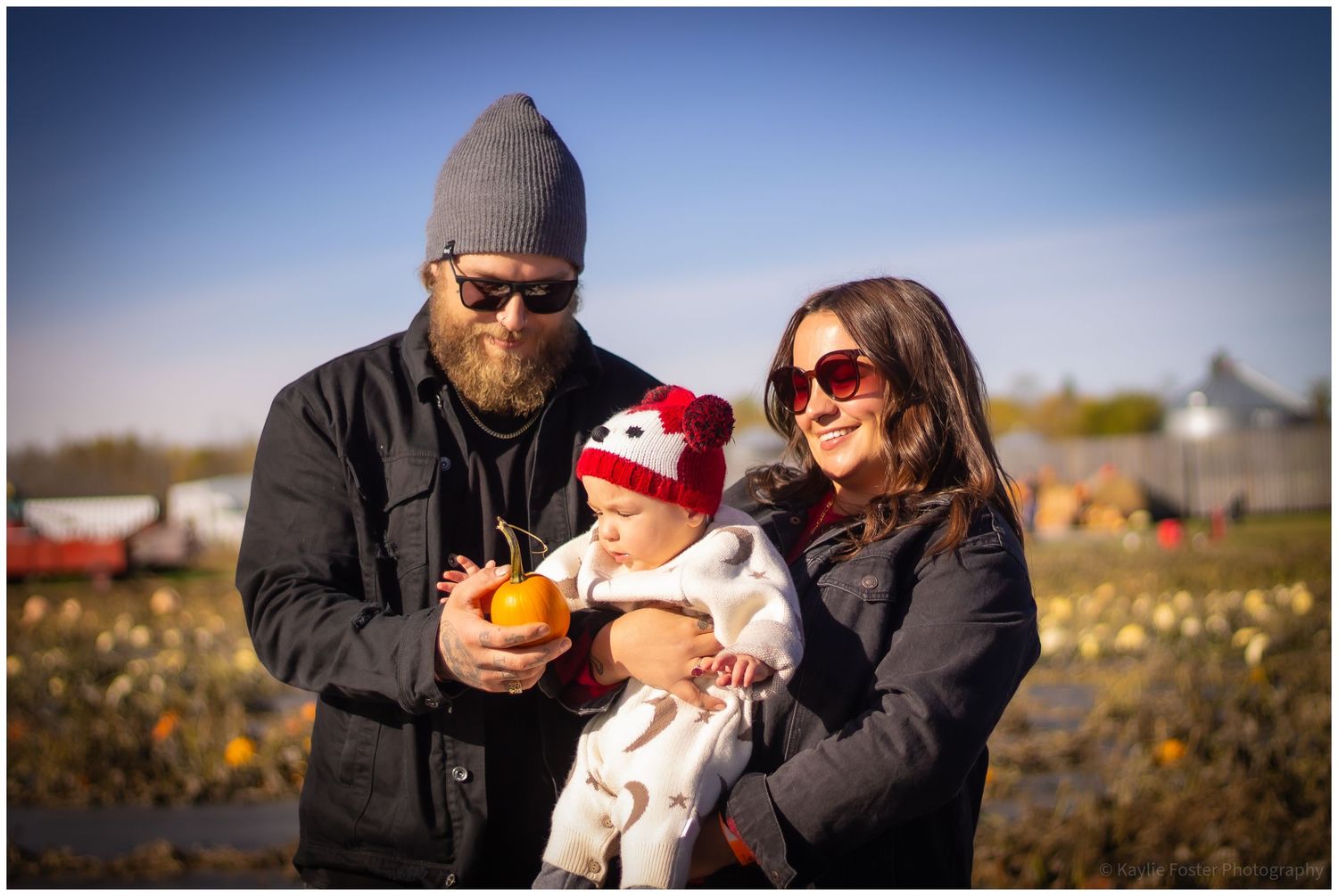 Family with baby picking pumpkins at a fall pumpkin patch on a sunny day.