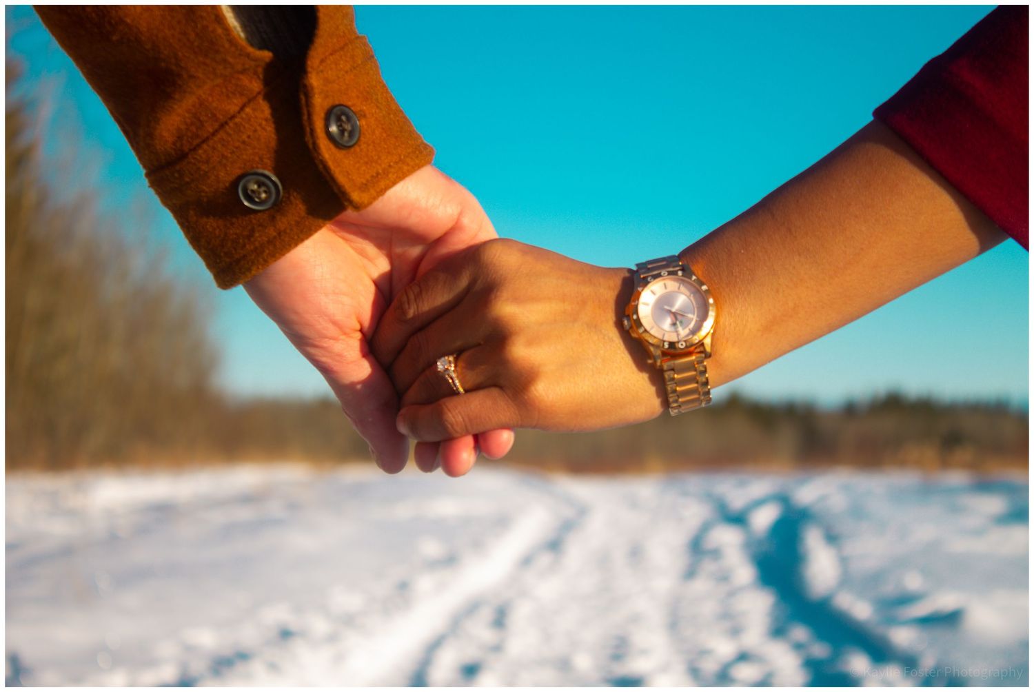 Two people holding hands in a snowy winter landscape, one wearing a gold watch, symbolizing love and connection.
