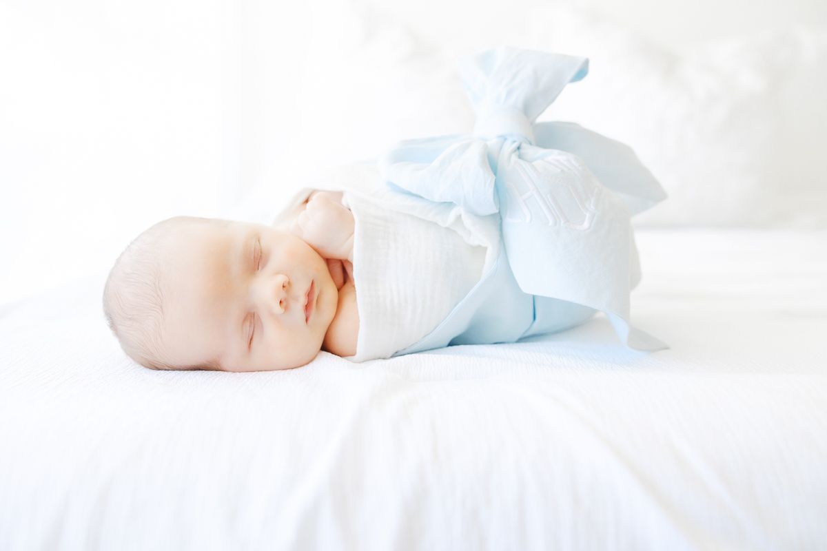 Peaceful newborn baby swaddled in white and blue blanket sleeping on white bedding.
