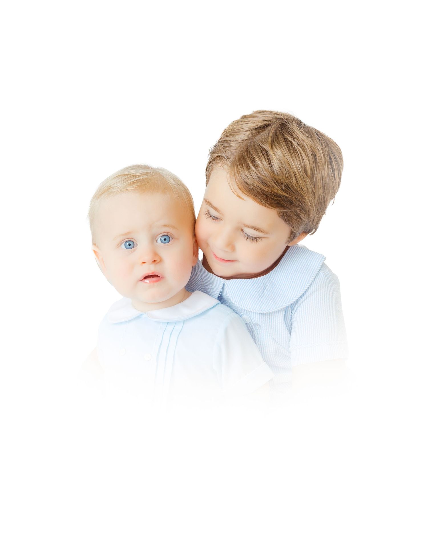 Older blonde boy gently hugging a wide-eyed baby sibling, both wearing matching light blue outfits.