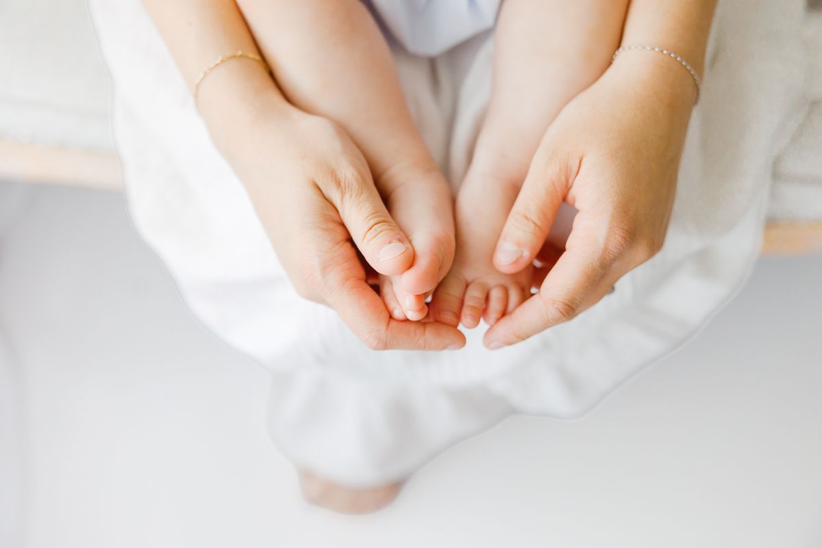 Adult hands gently cradling tiny newborn baby feet, captured from above on a white background.