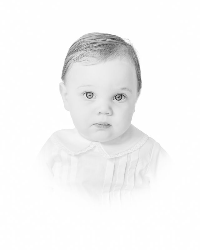 Black and white portrait photo of a baby with big eyes wearing a white collared outfit, soft vignette style.