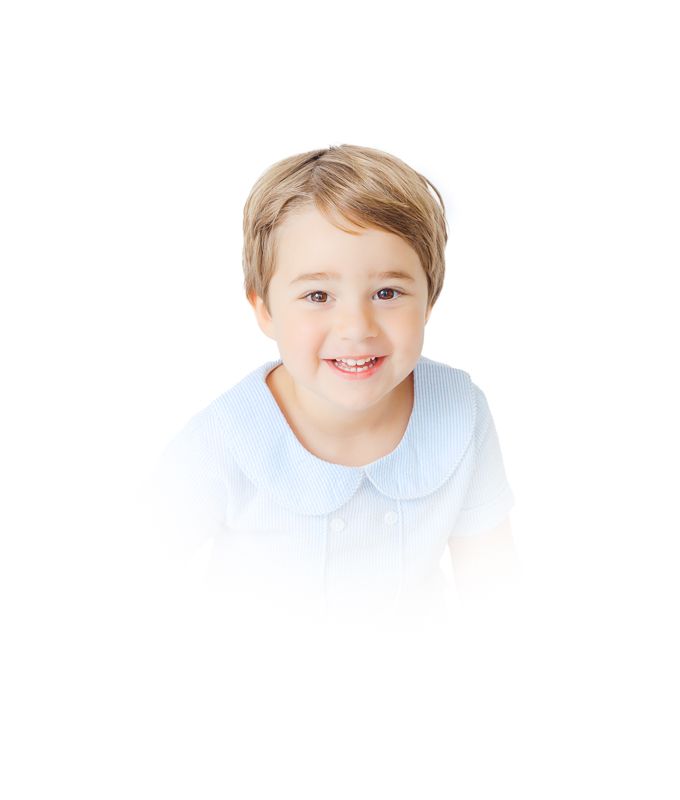 Smiling young boy with blonde hair wearing a light blue Peter Pan collar shirt against a white background.