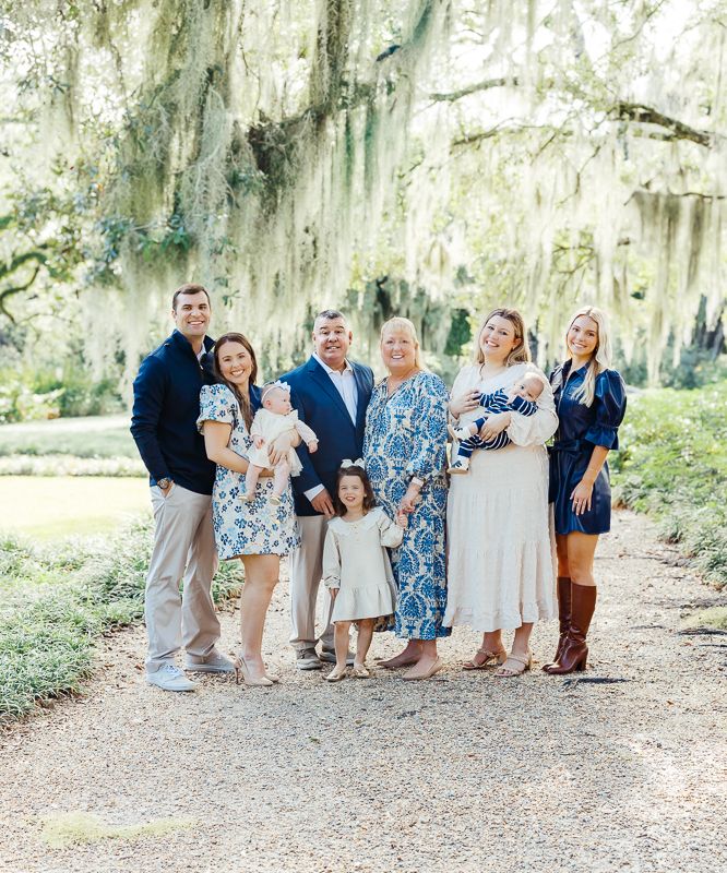 Large family group portrait outdoors under Spanish moss-draped oak trees on a scenic garden path.