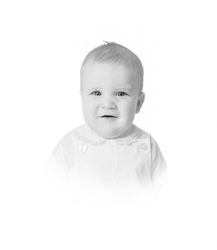 Black and white portrait of a smiling baby wearing a white collared outfit, soft studio photography.