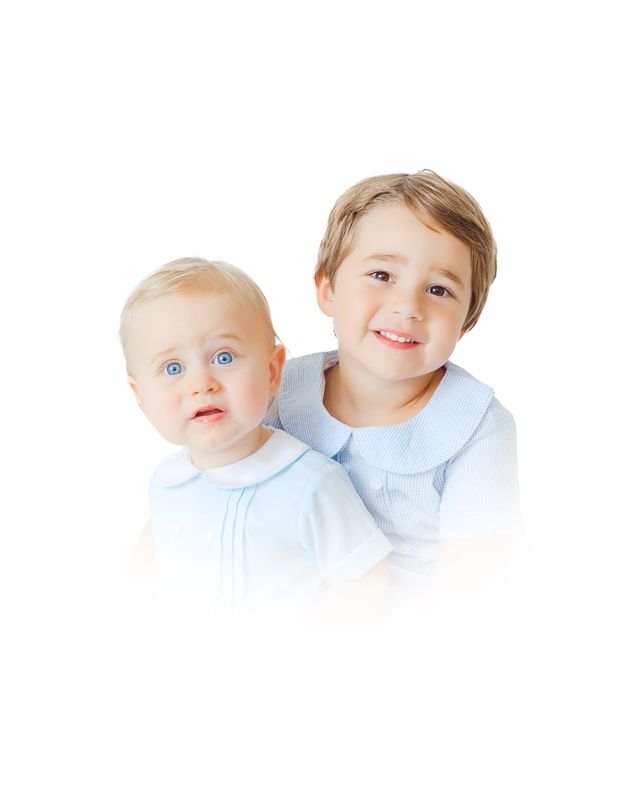 Two young brothers in light blue outfits, a smiling toddler and a blue-eyed baby, posing together on white background.
