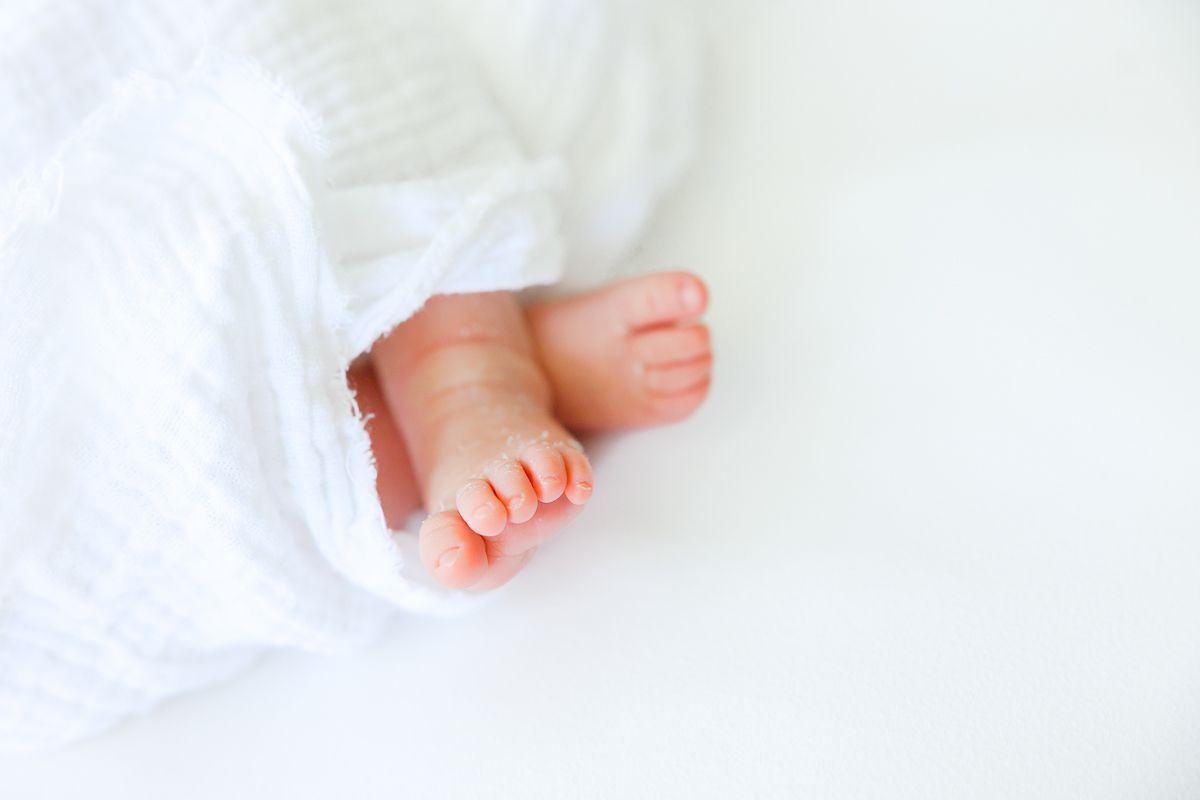 Close-up of tiny newborn baby feet wrapped in a soft white blanket on a white background.