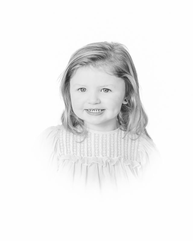 Black and white portrait photo of a smiling young girl with shoulder-length hair wearing a smocked dress.