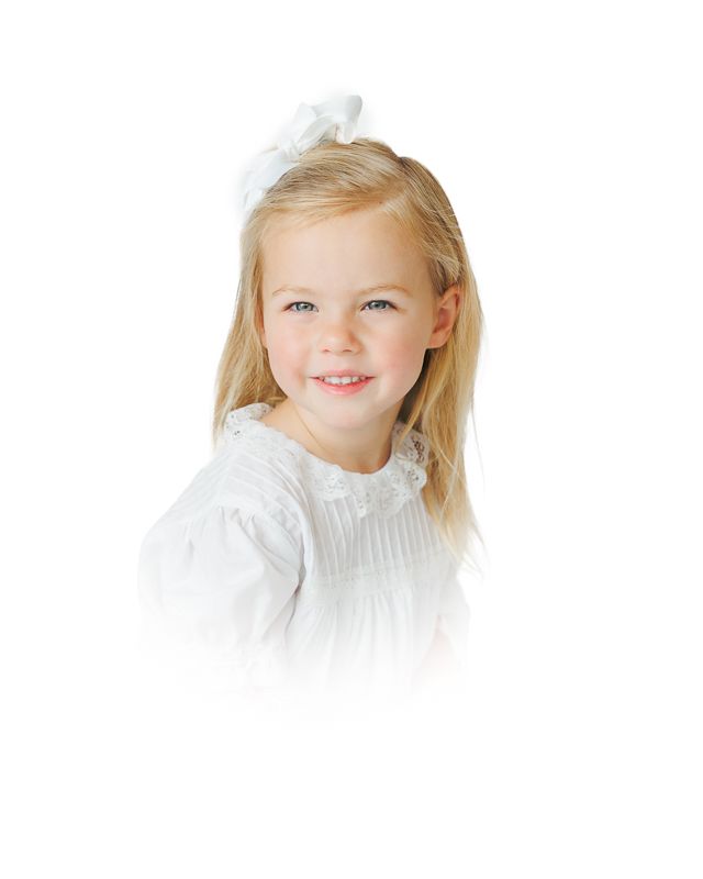 Young girl with blonde hair and white bow smiling, wearing a white dress against a white background.