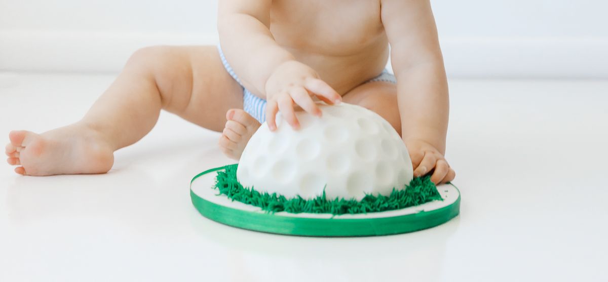 Baby smashing a white fondant cake with green grass decoration during a first birthday smash cake photoshoot.