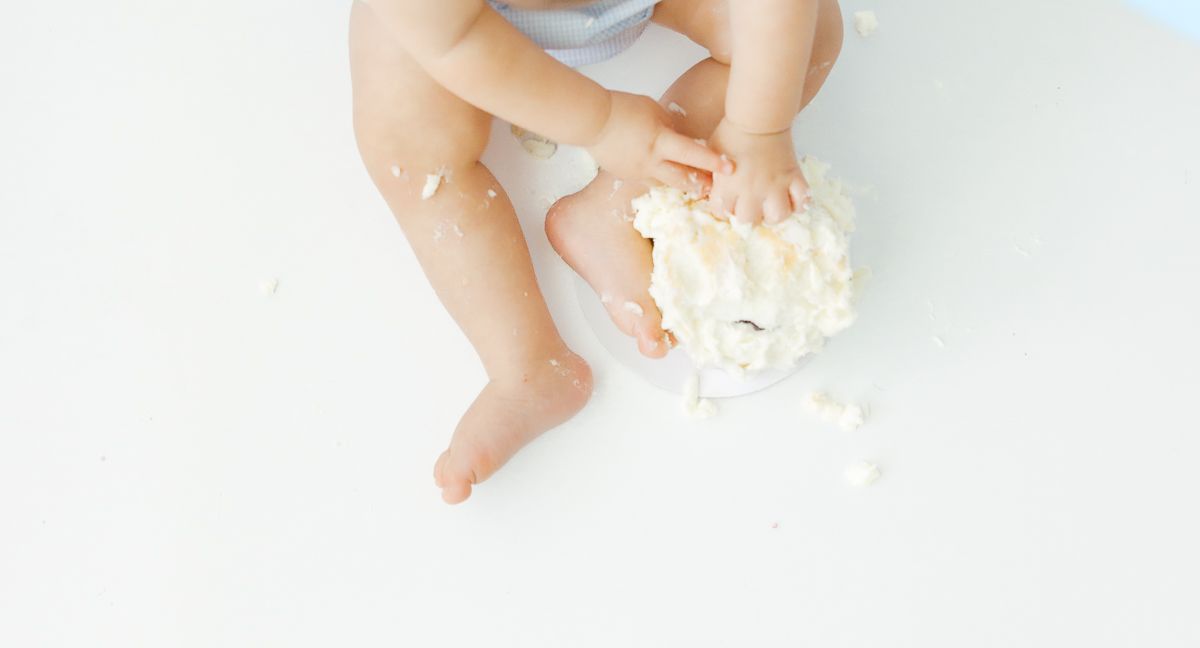 Baby smashing white cake with hands during first birthday cake smash photo session on white background.