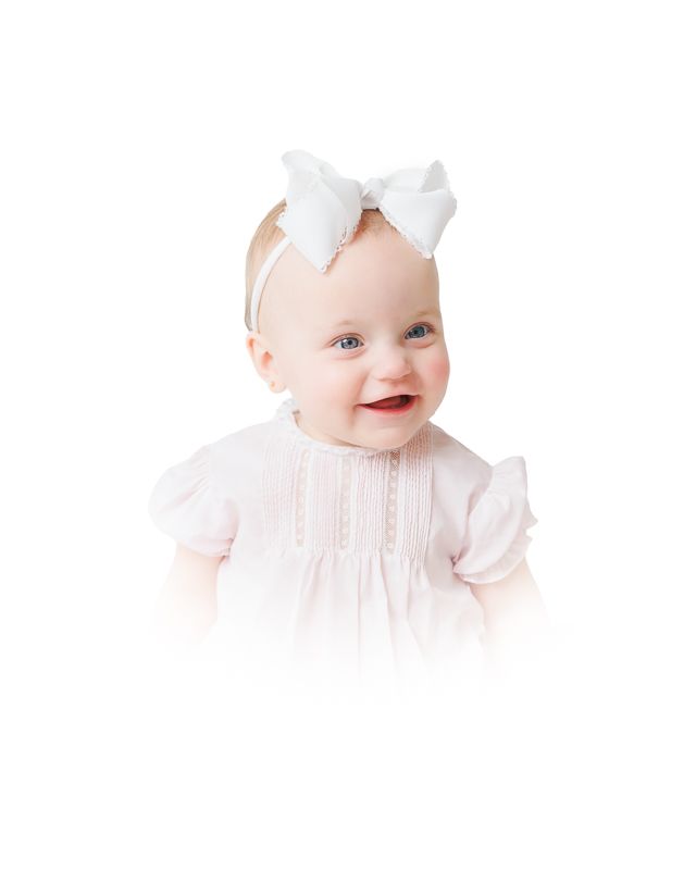 Smiling baby girl wearing a white bow headband and pink ruffle dress on a white background.
