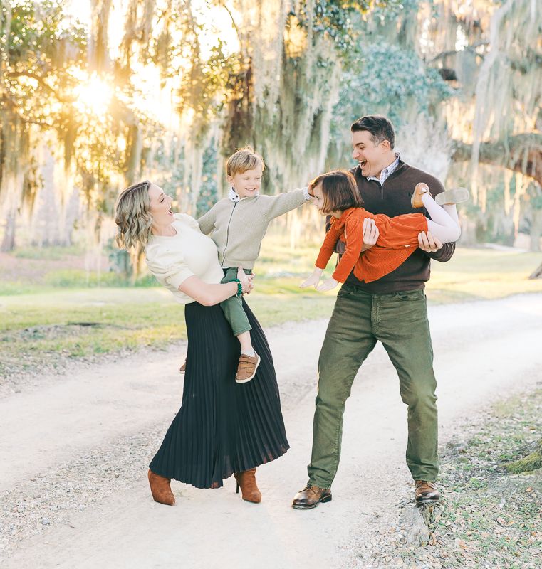 Family of four playing outdoors at golden hour among moss-draped trees on a sunlit path.