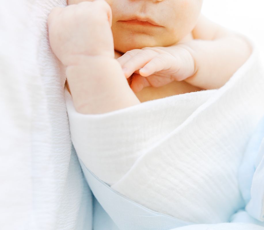 Close-up of a peaceful newborn baby wrapped in a soft white blanket, with tiny hands visible near face.