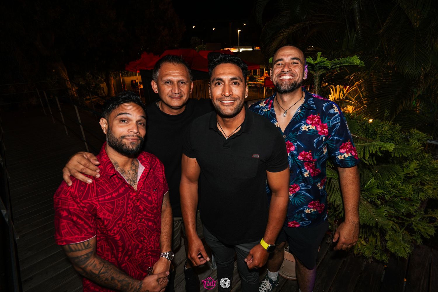 Four men smiling and posing together outdoors at a nighttime social gathering.