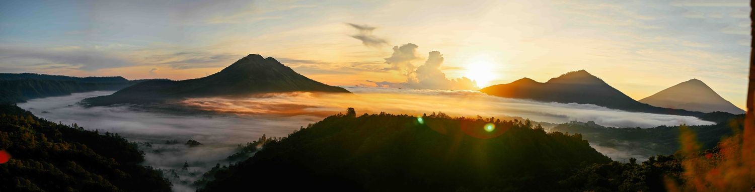 Panoramic sunrise view over volcanic mountains with misty valleys and golden sky in Bali, Indonesia.