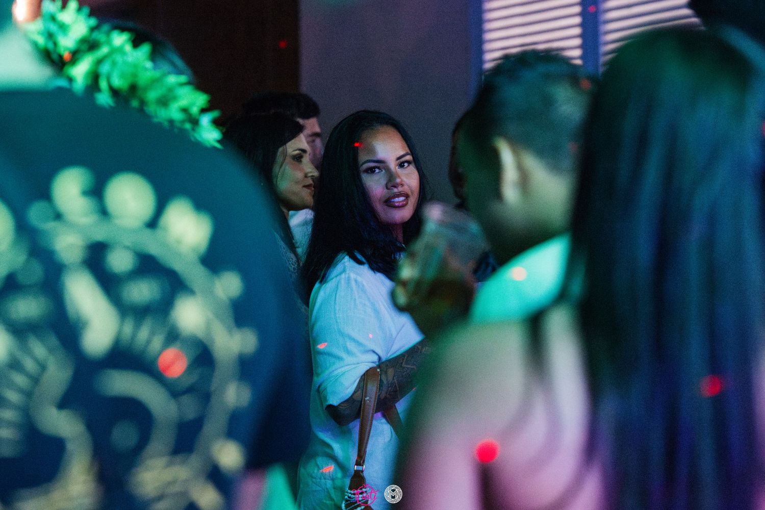 Young women socializing at a vibrant nightclub party with colorful green and blue lighting.