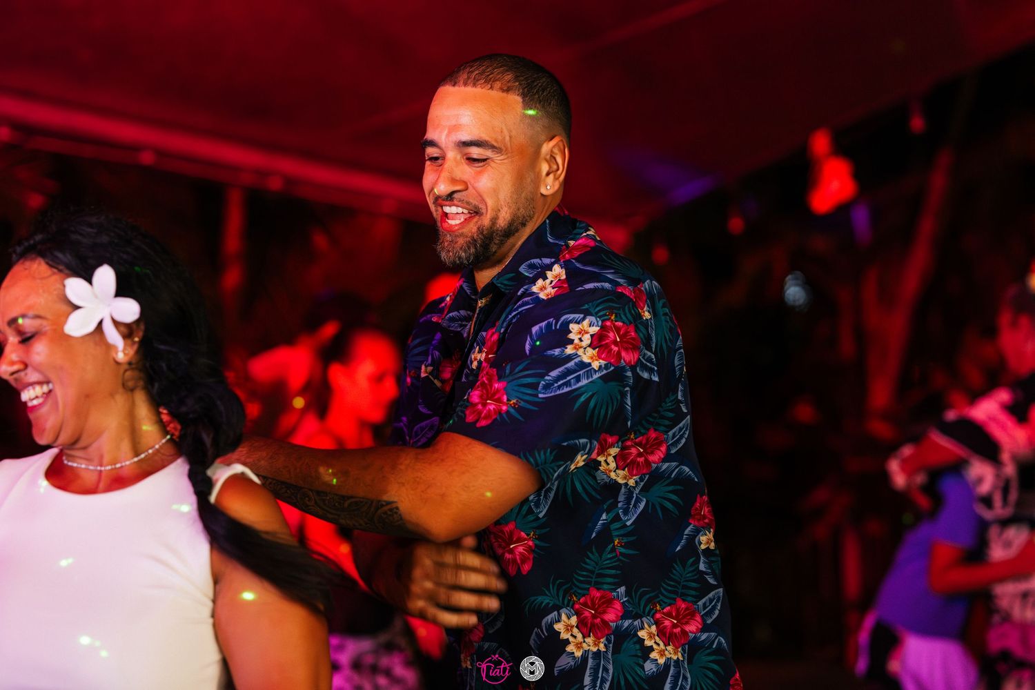 Man in floral shirt dancing joyfully with a woman at an outdoor night party.