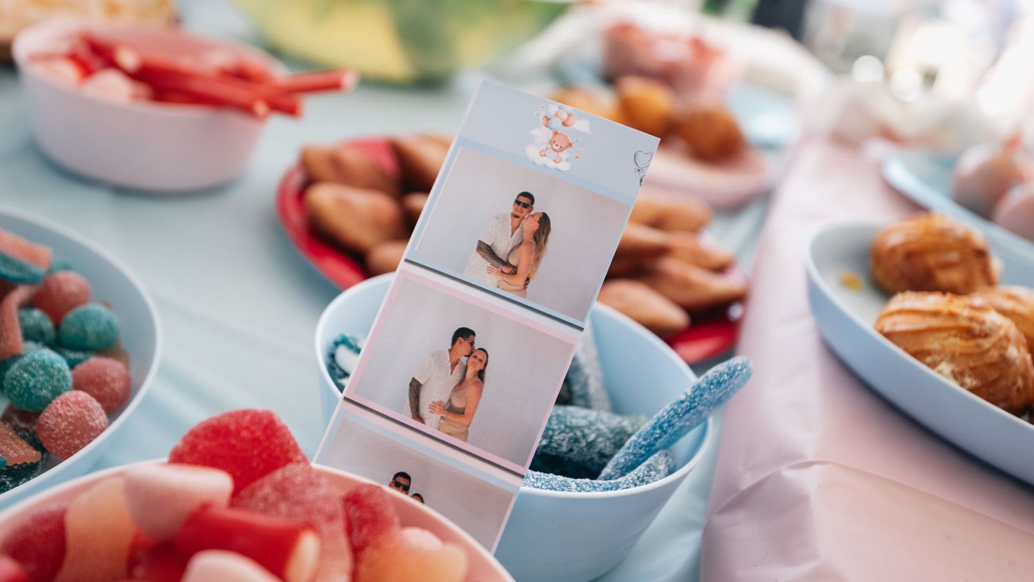 Colorful candy table display with photo booth strip pictures surrounded by gummy bears and pastries.