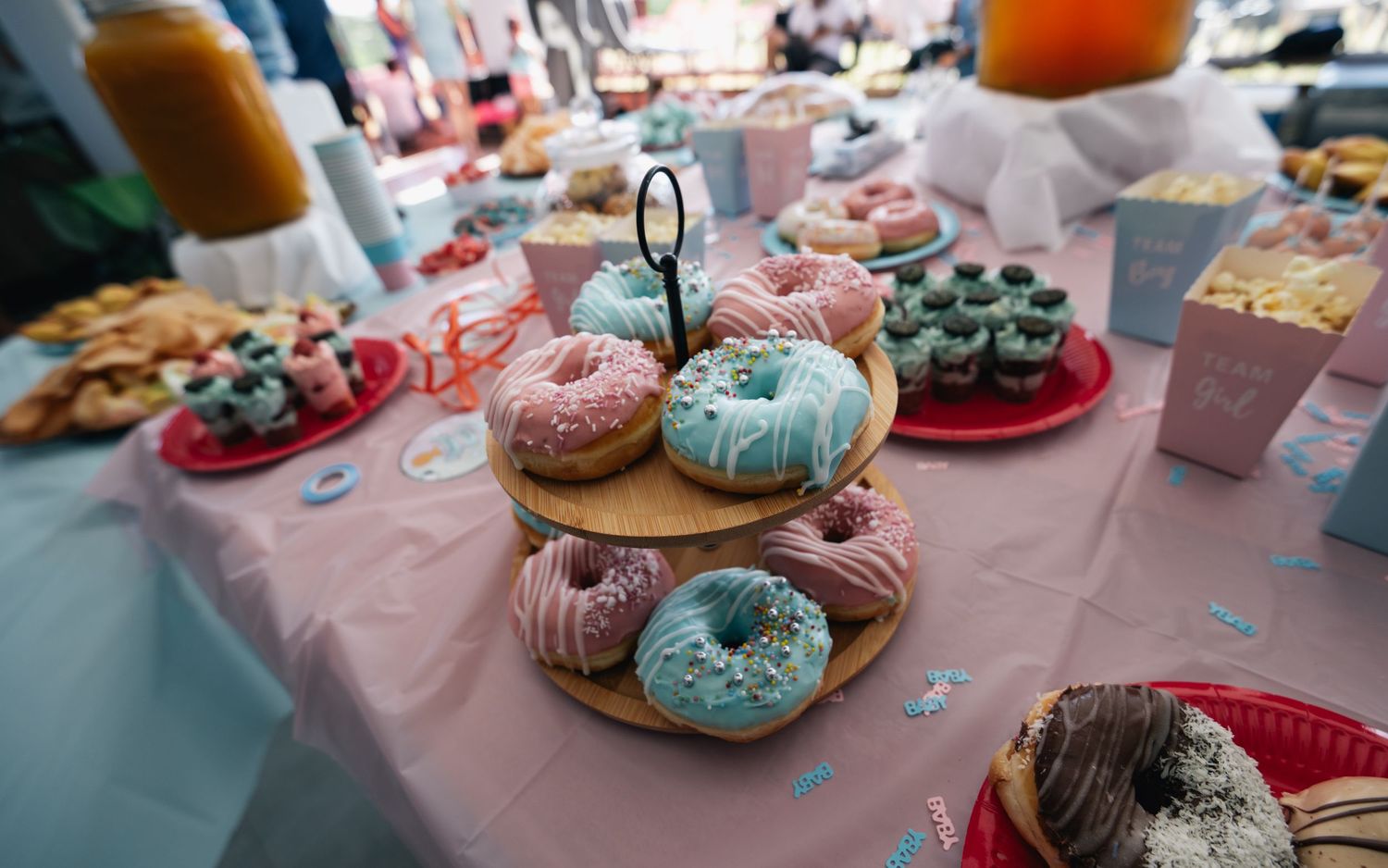 Colorful pink and blue frosted donuts displayed on tiered stand at gender reveal party.