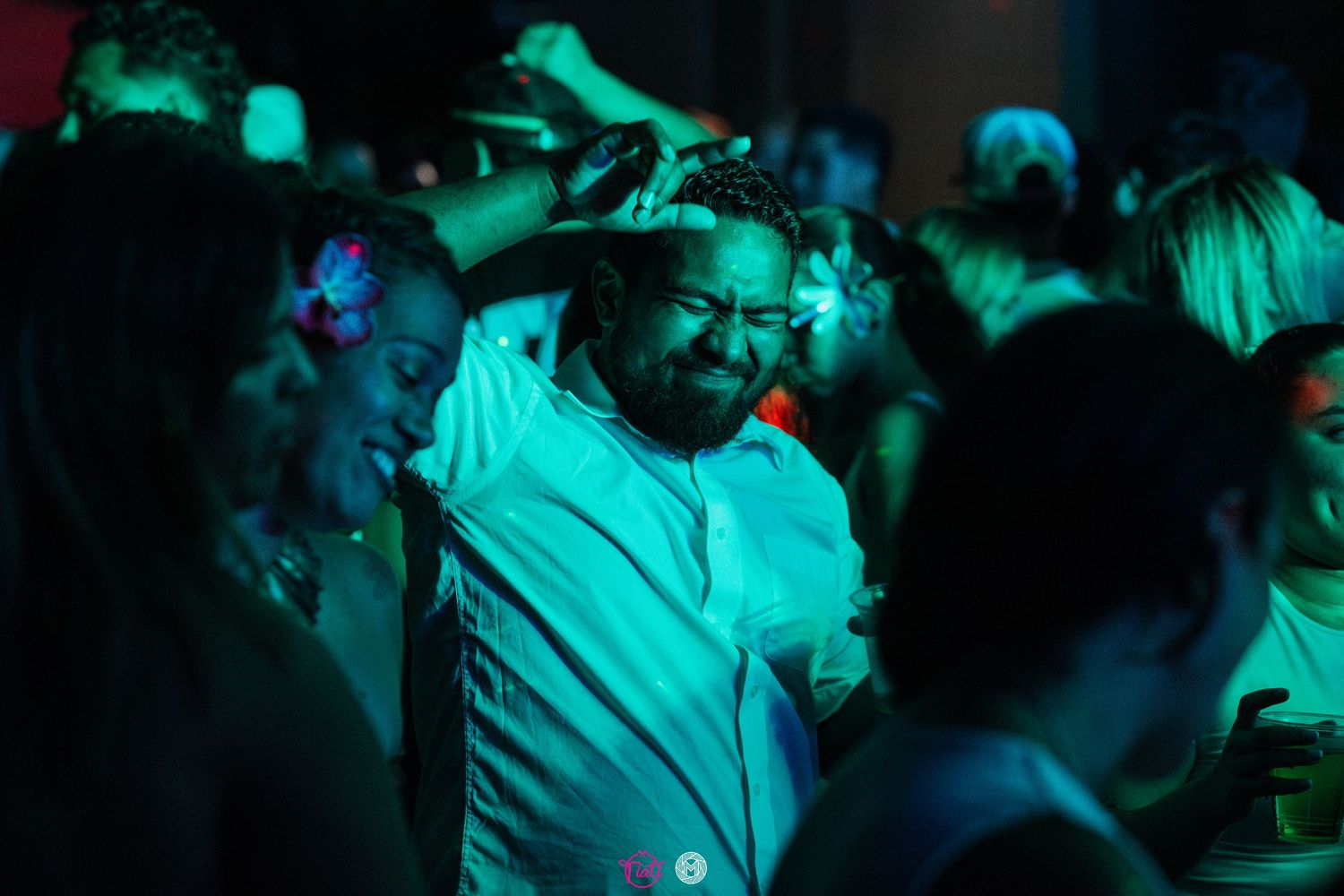 Man in white shirt dancing in a crowd under teal lighting at a nighttime event.