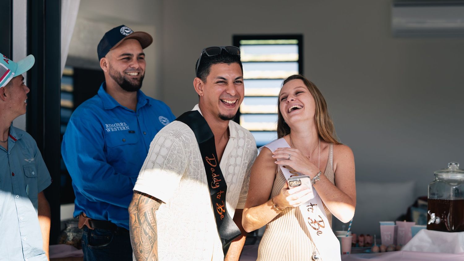 Three people laughing and smiling together indoors during a casual celebration event.