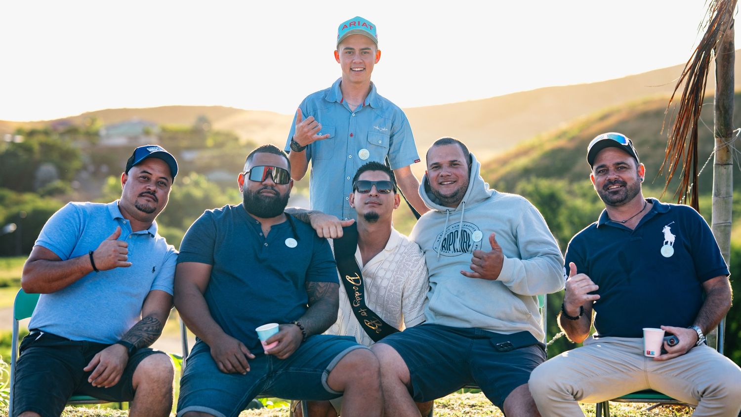 Group of six men posing together on green hillside during outdoor social gathering.