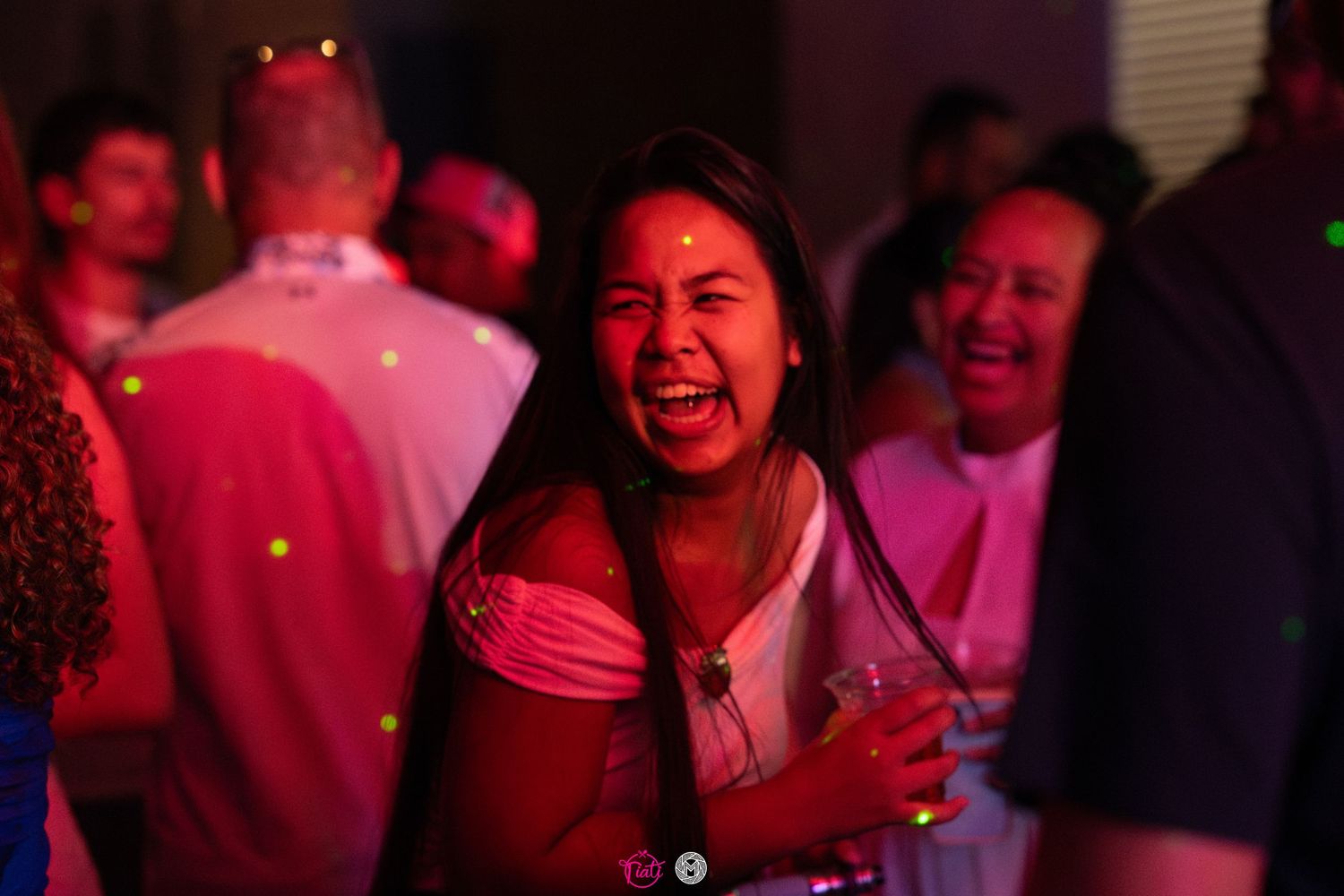 Woman laughing joyfully while holding a drink under pink lighting at a night party.