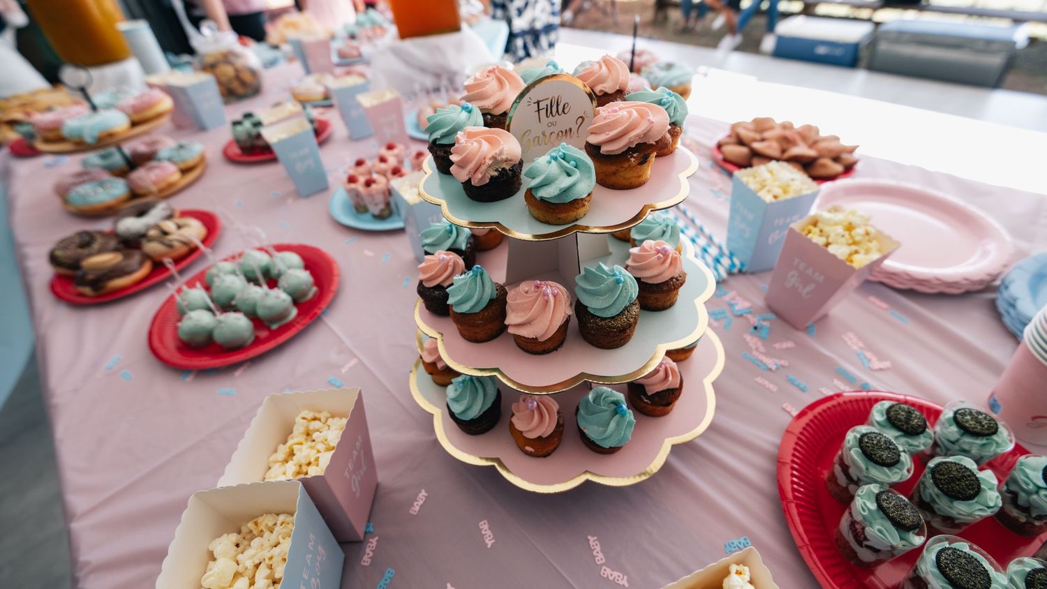 Three-tier cupcake stand with pink and blue frosted cupcakes on decorated dessert table.