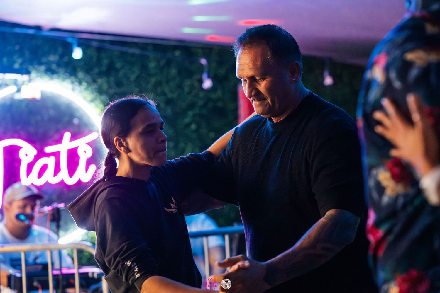 Couple dancing together near a neon sign at an elegant outdoor evening event.