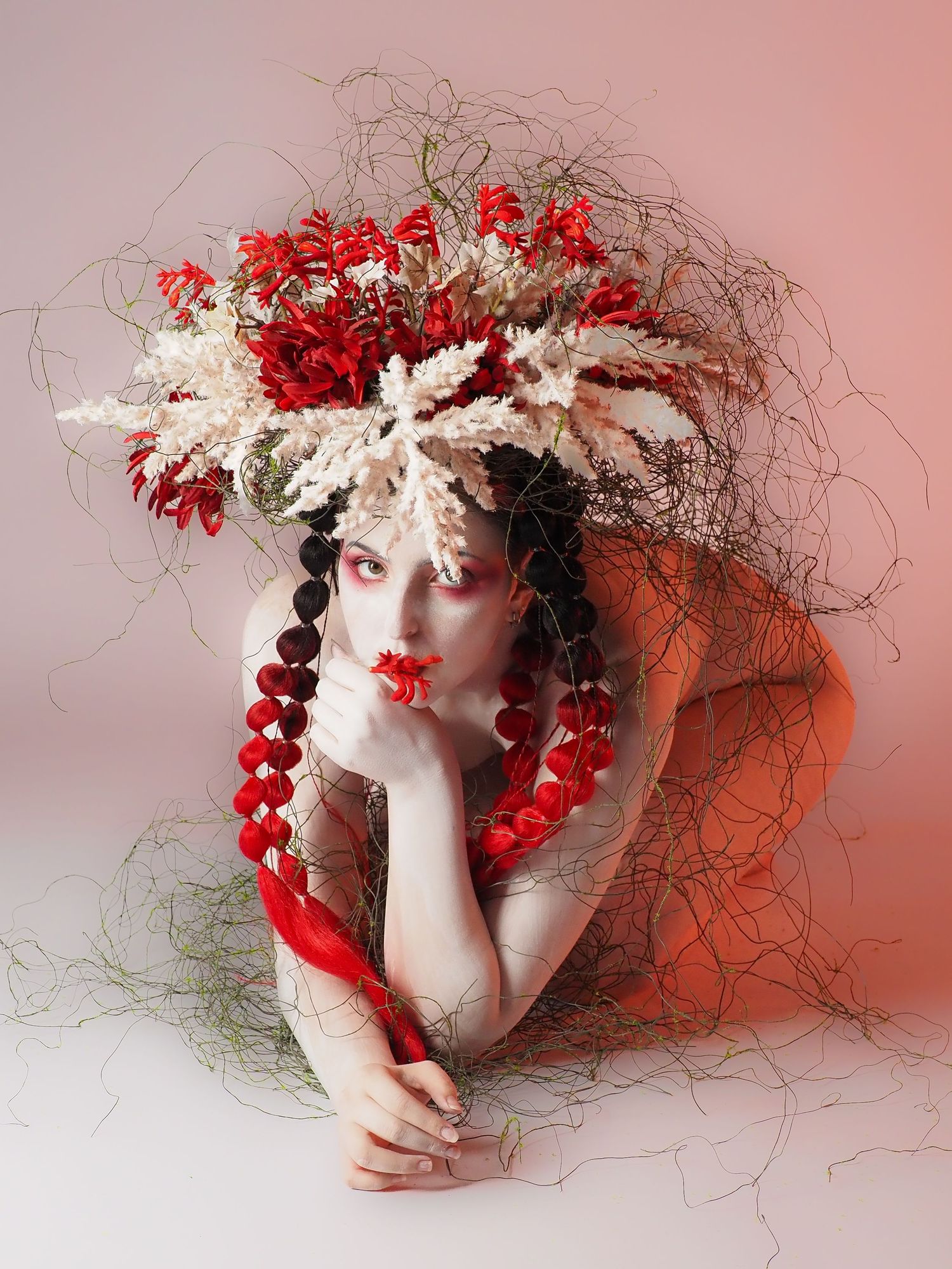 Artistic portrait of model wearing elaborate red and white floral crown with red bead necklace.
