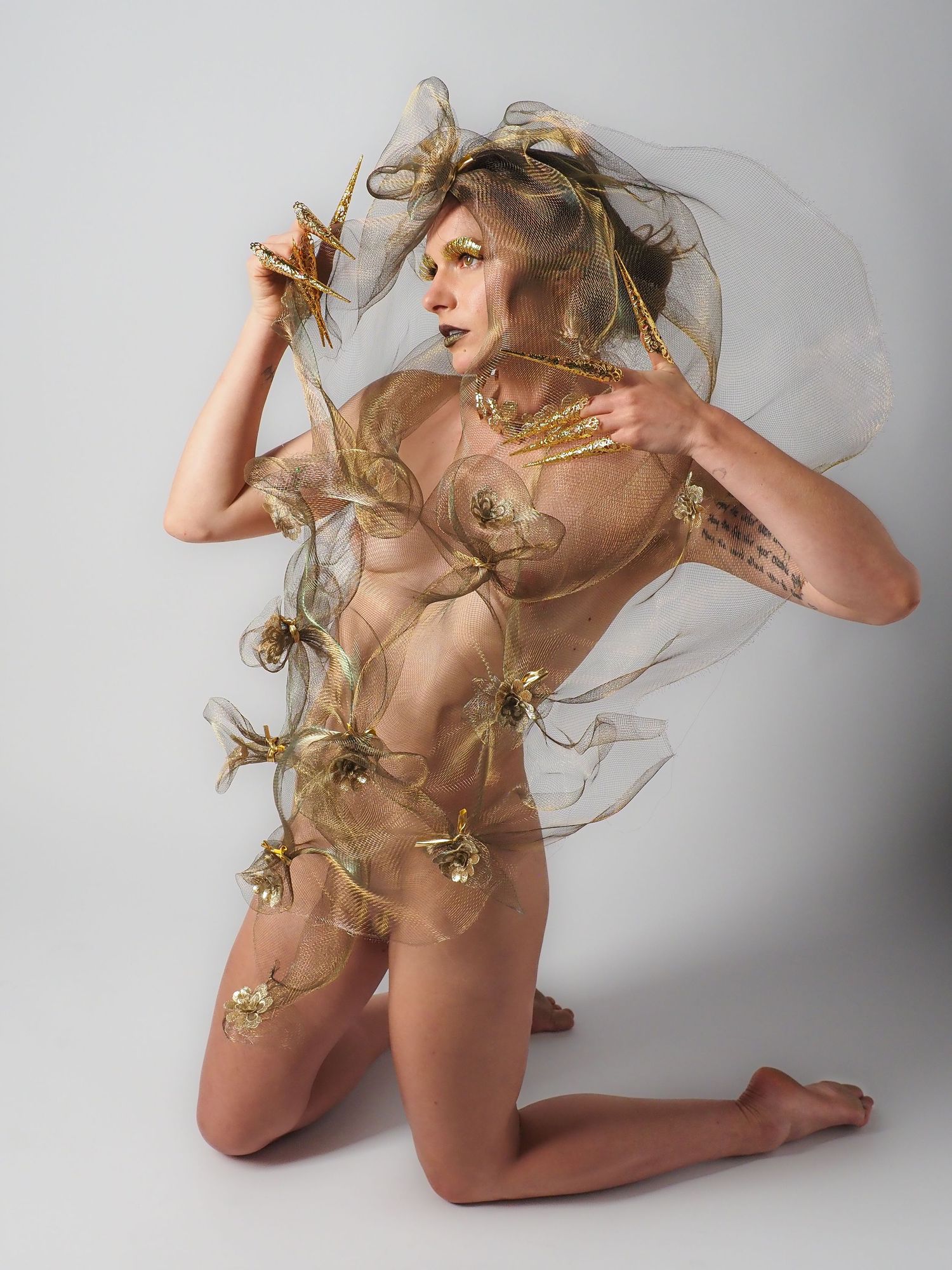 Fine art studio portrait of model wrapped in golden tulle with ornate gold insect accents.