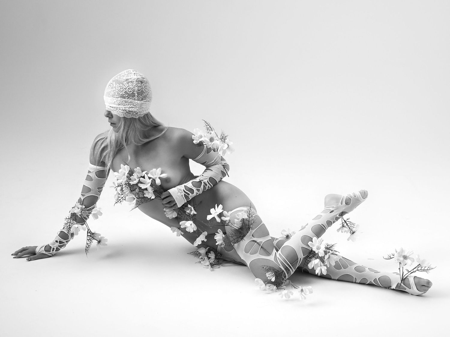 Black and white artistic photo of woman adorned with white flowers posing on floor.