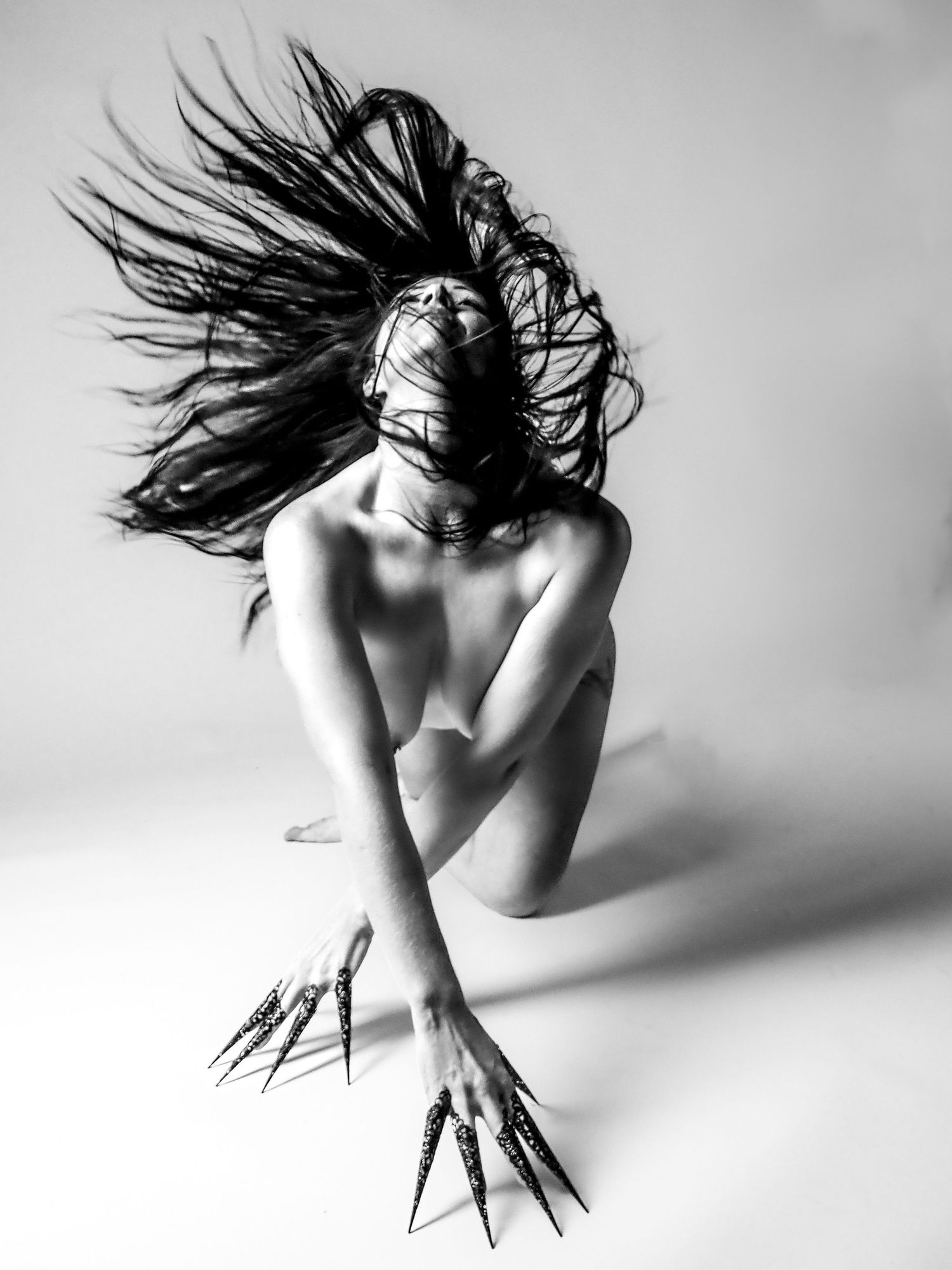 Black and white artistic nude with wild flowing hair and long black talon-like nail extensions.