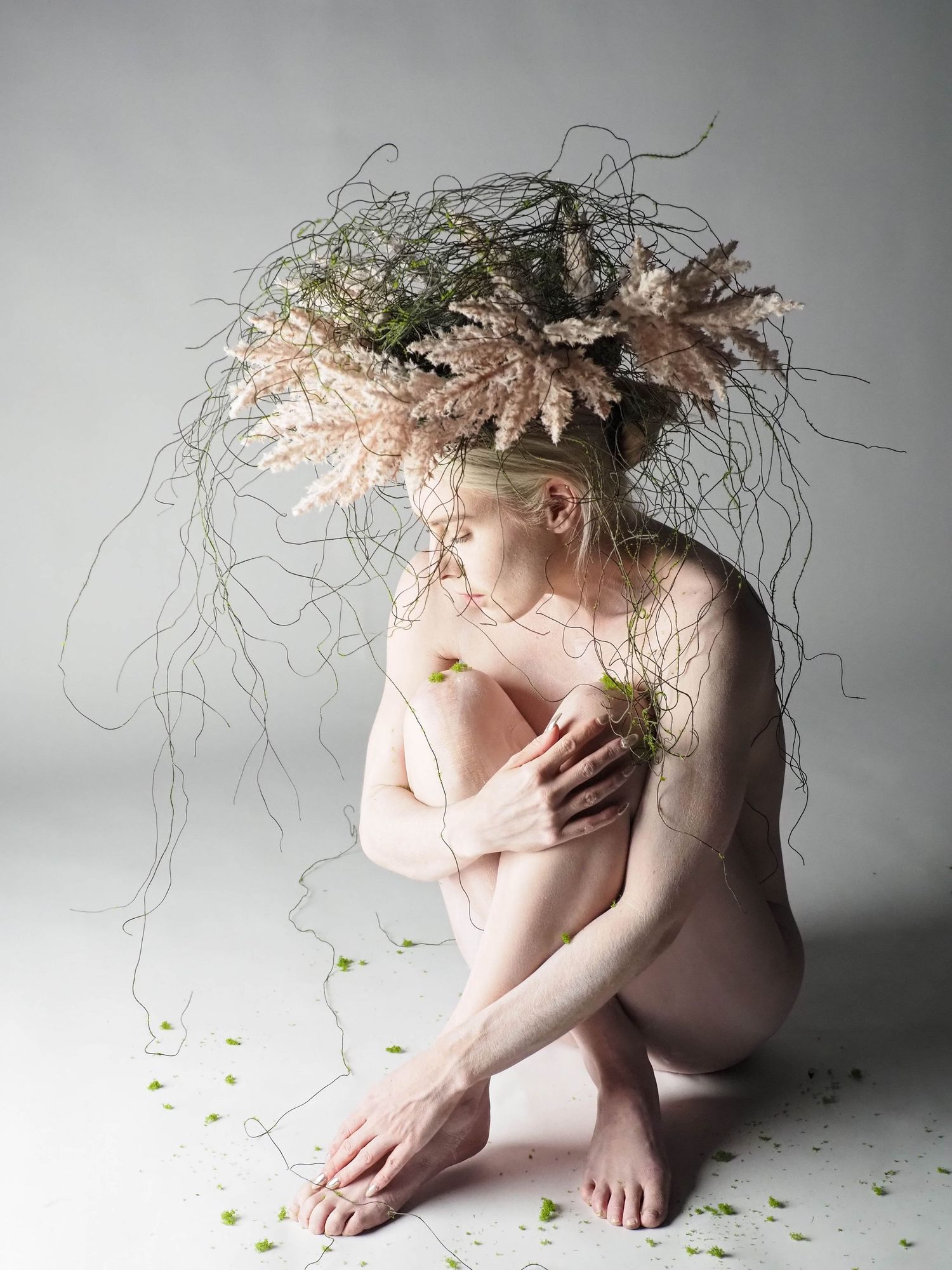 Fine art nude woman wearing an elaborate floral botanical headdress with trailing greenery on white.