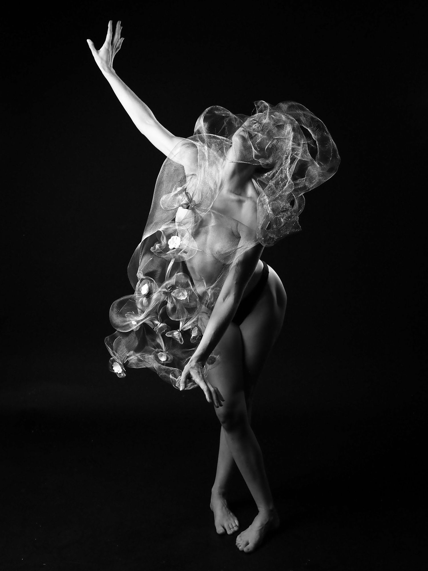 Black and white artistic nude dancer wrapped in flowing sheer fabric mid-motion.