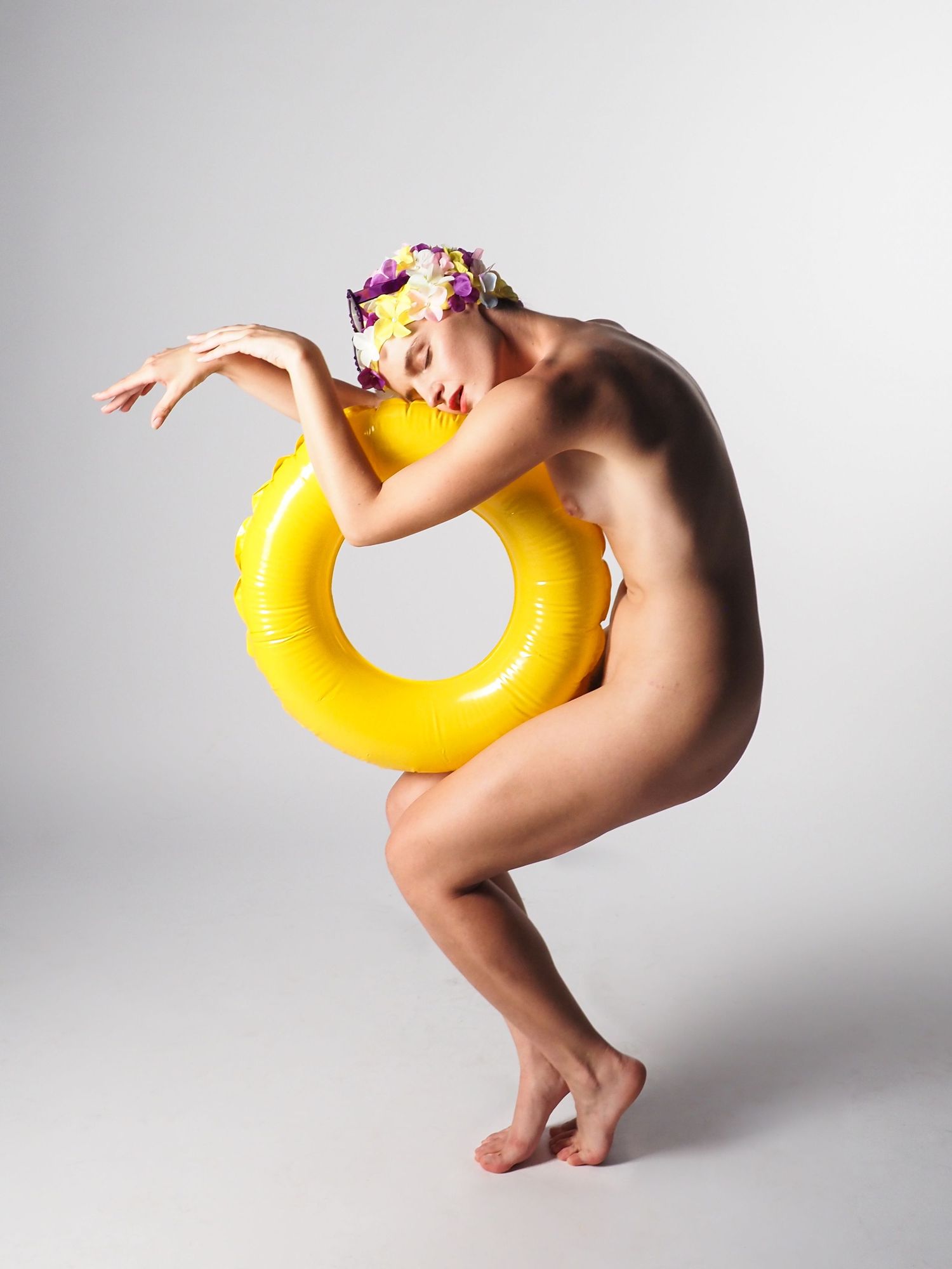 Nude woman posing with yellow inflatable pool ring and floral swim cap.