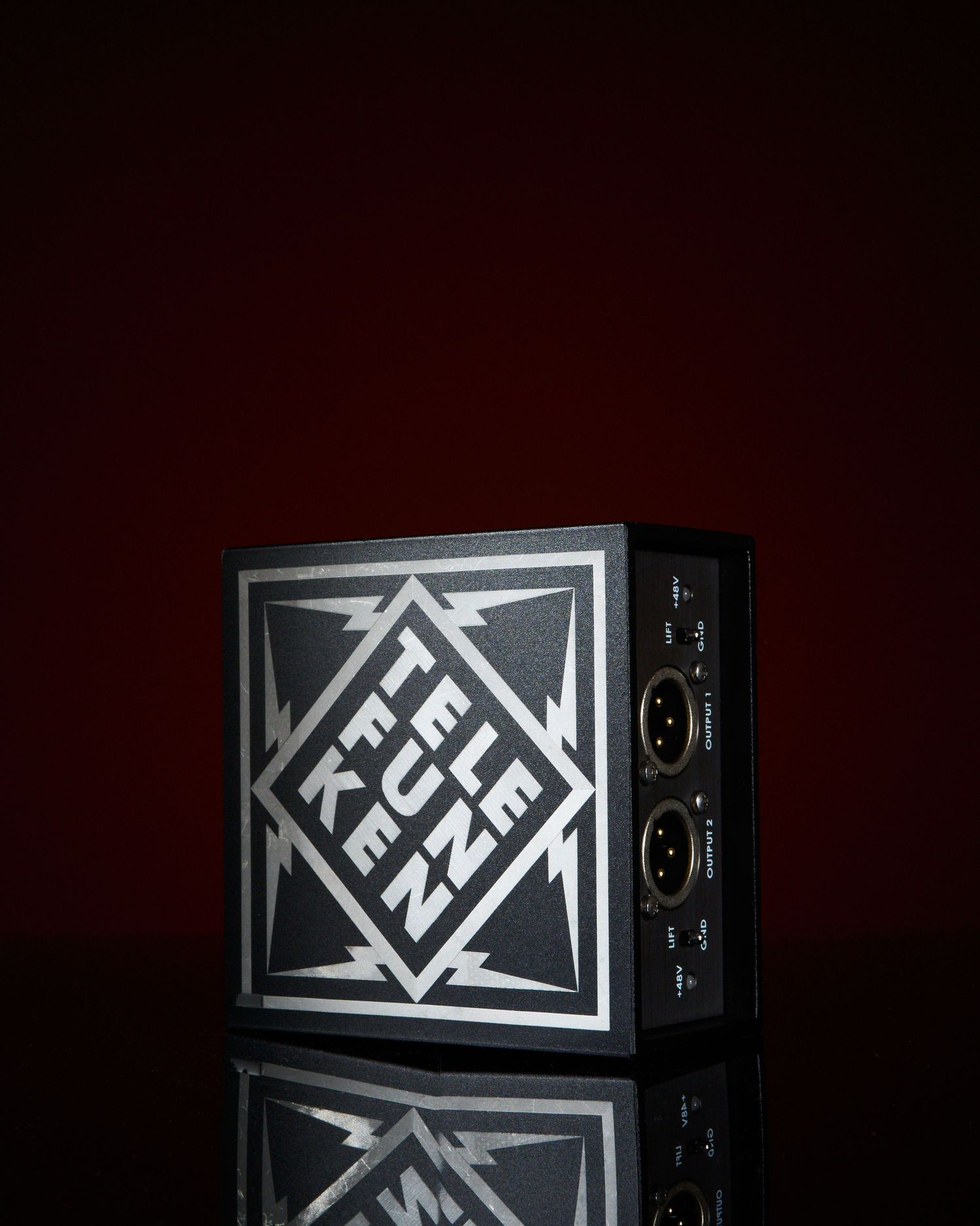 Telefunken black audio equipment box with geometric logo and XLR connectors on dark red background.