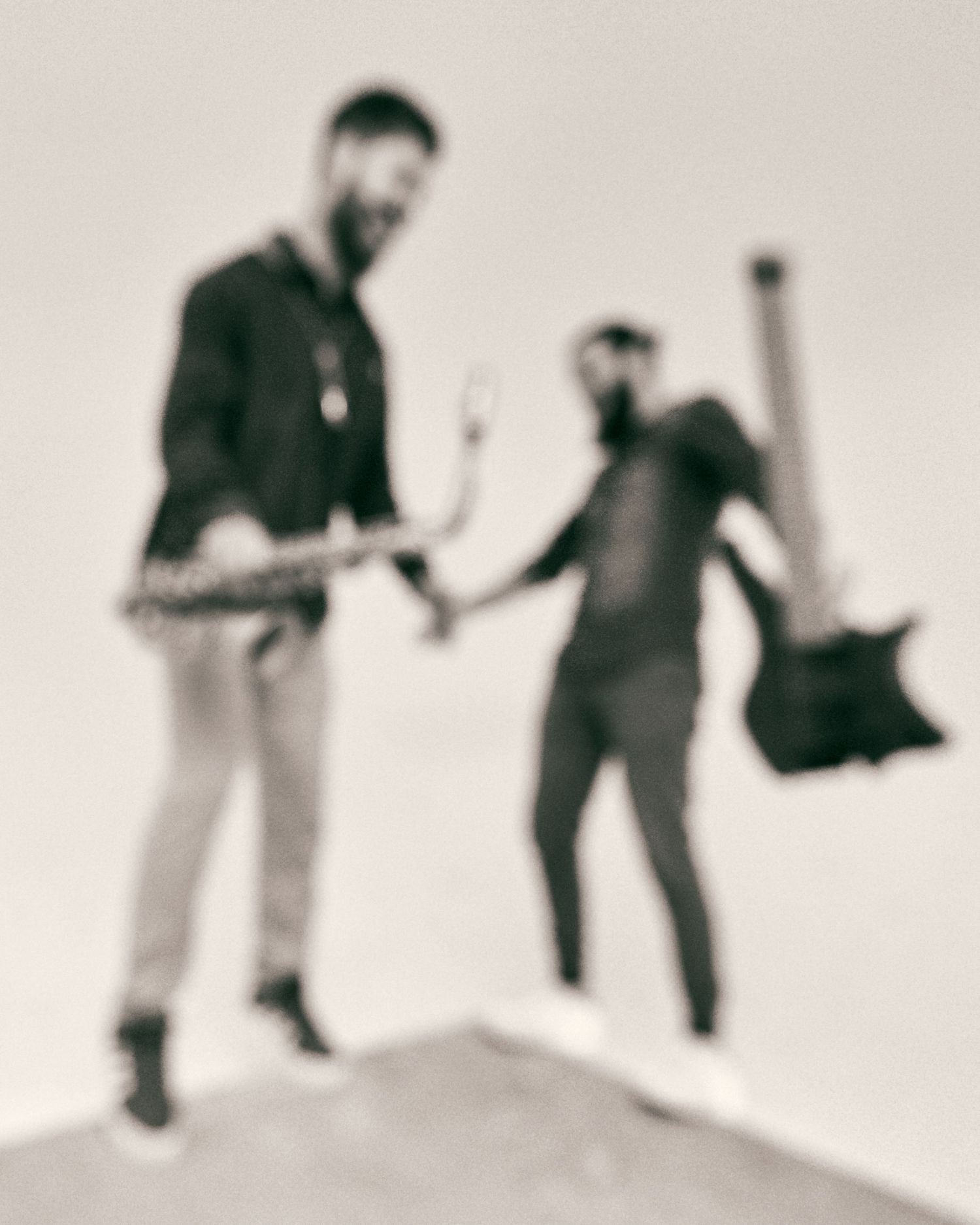 Two blurred figures holding guitars jumping outdoors in vintage sepia toned photo.