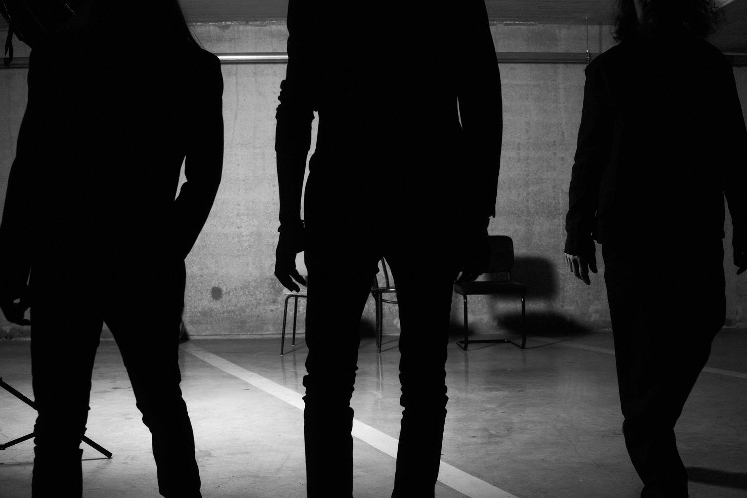 Silhouettes of three people standing in a dimly lit industrial space in black and white.