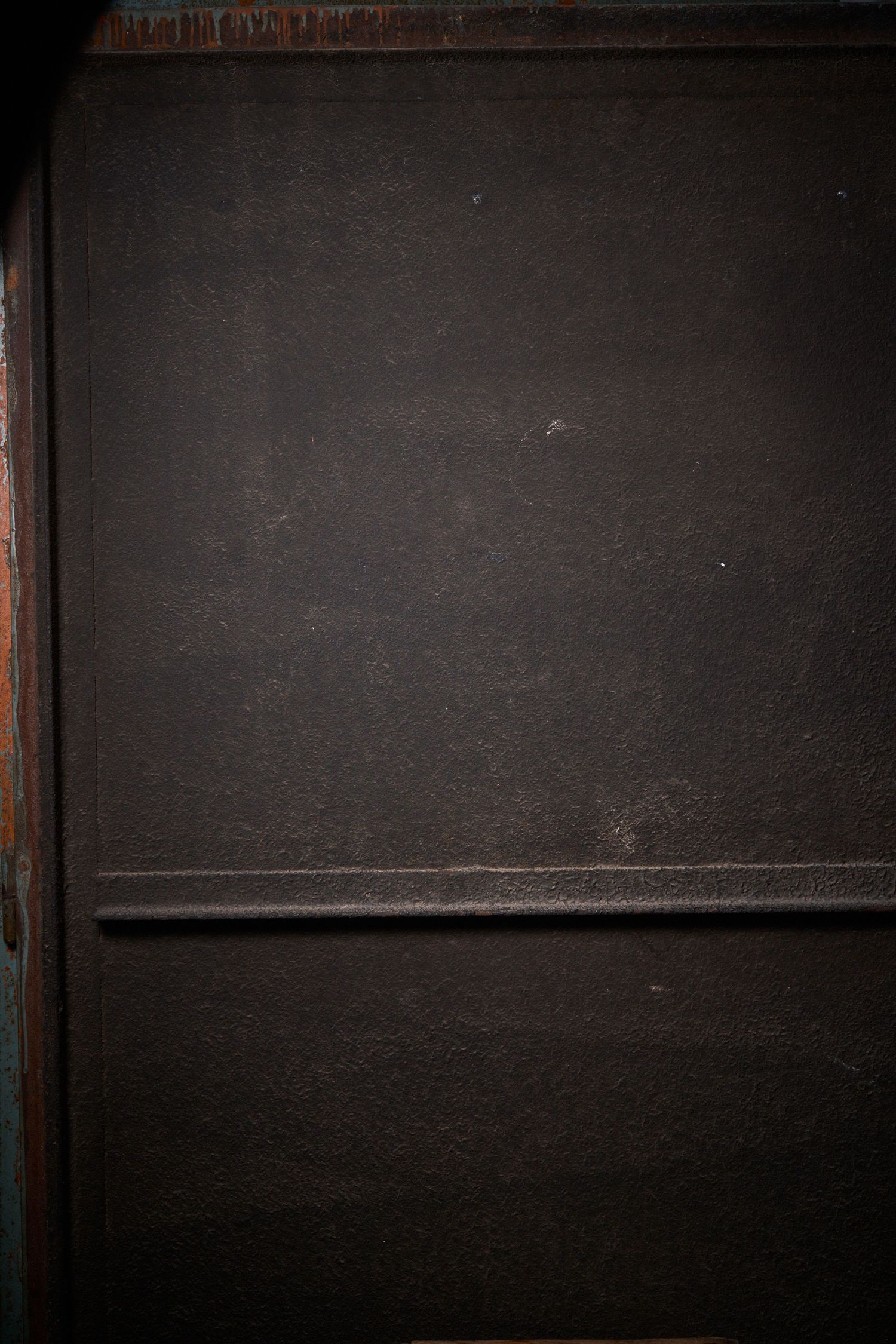 Dark vintage metal door panel with worn texture and horizontal rail detail in dim lighting.
