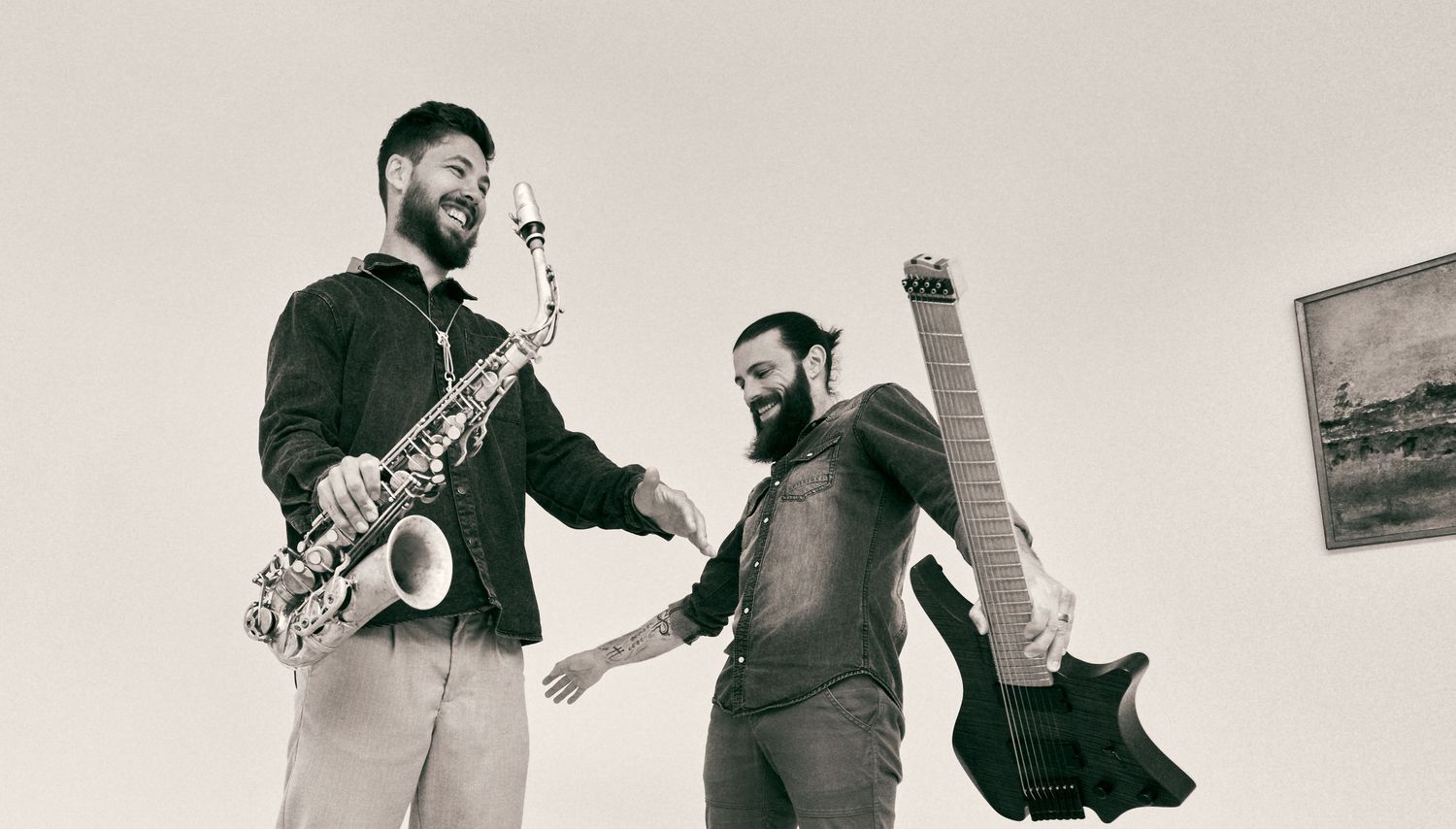 Two musicians laughing with saxophone and bass guitar outdoors.