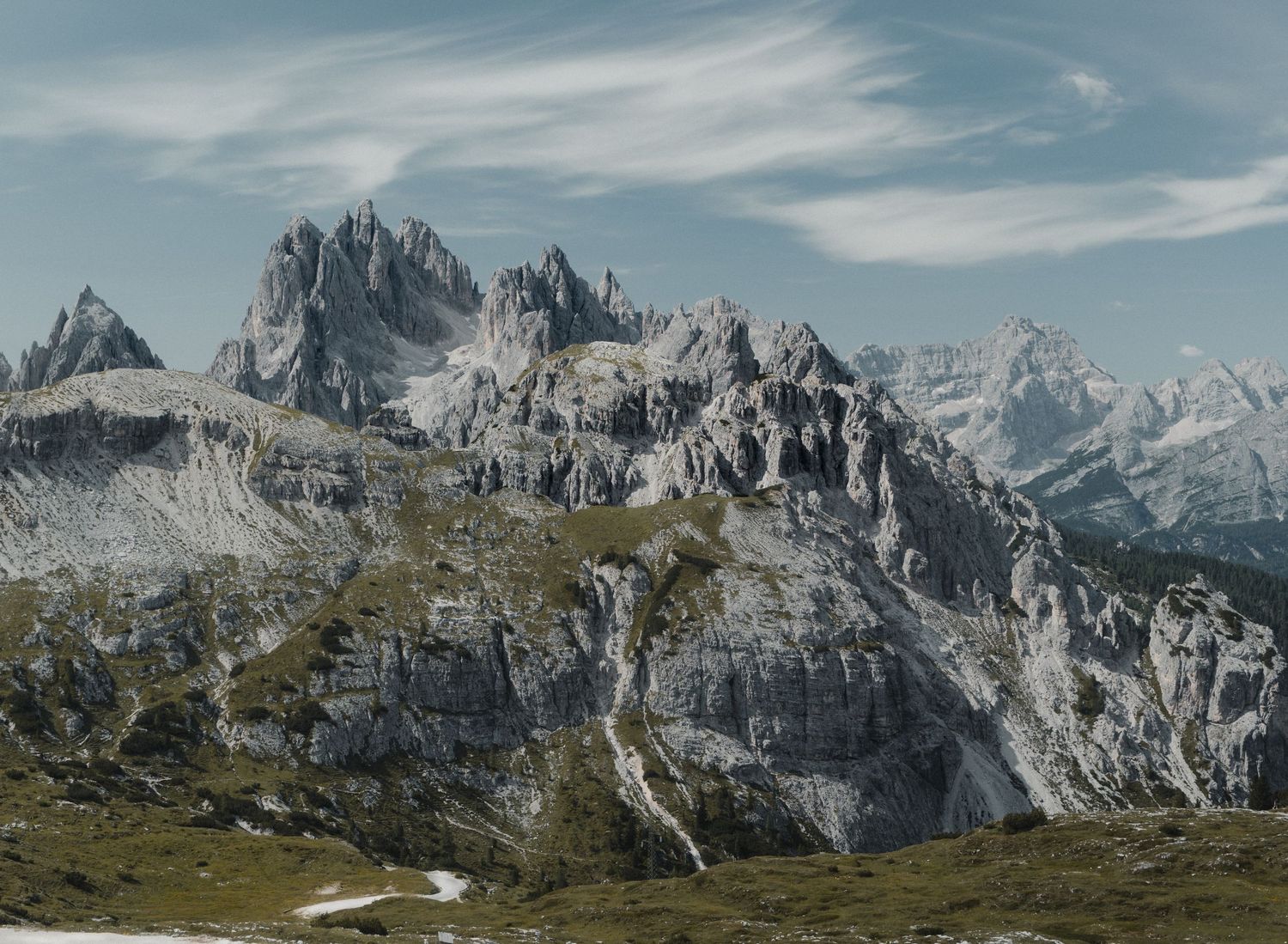 Dramatic rocky Dolomite mountain peaks rise against a partly cloudy sky in the Italian Alps.